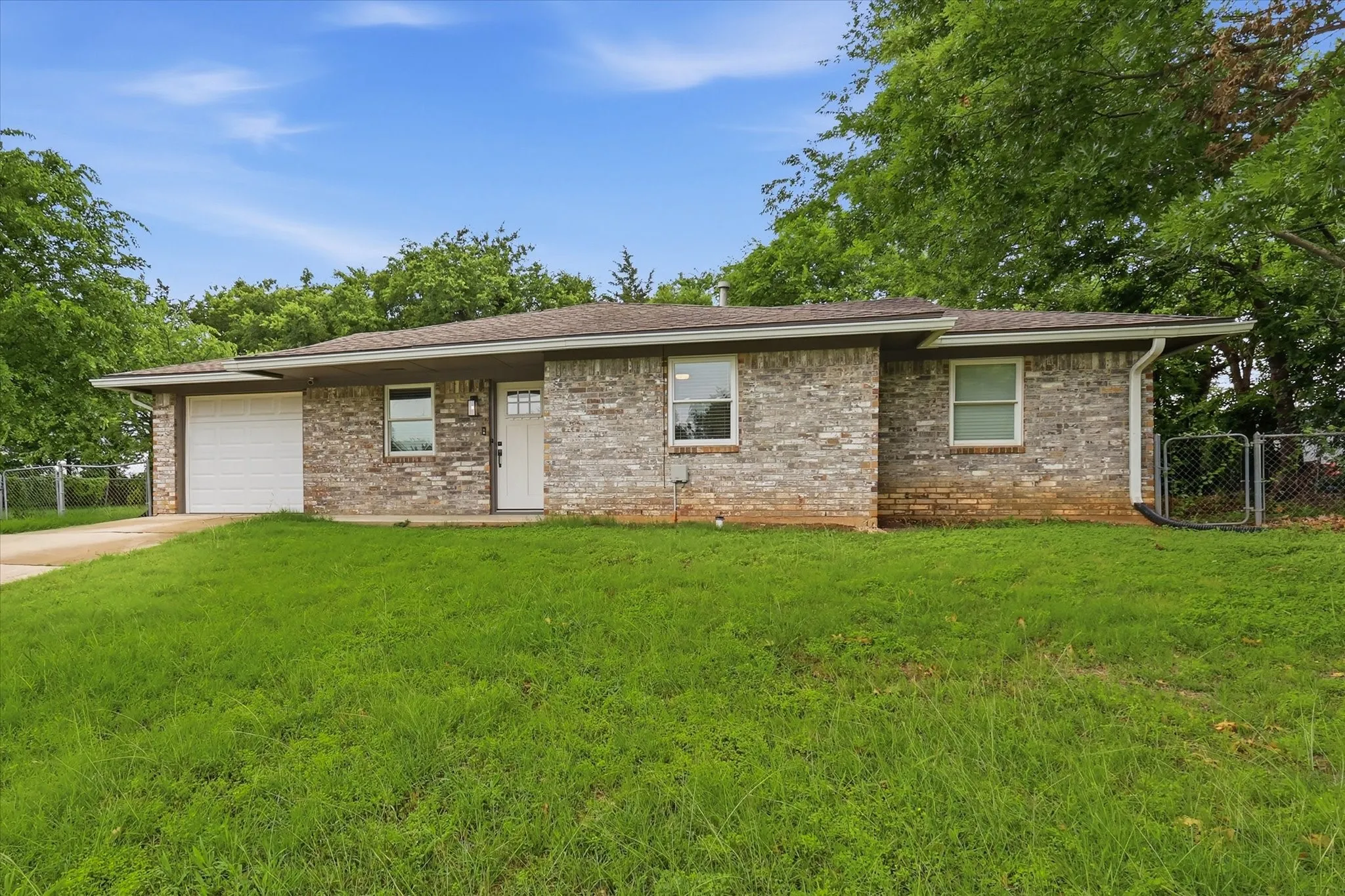 Brick exterior with a white entry door, an attached garage, and a chain-link fence