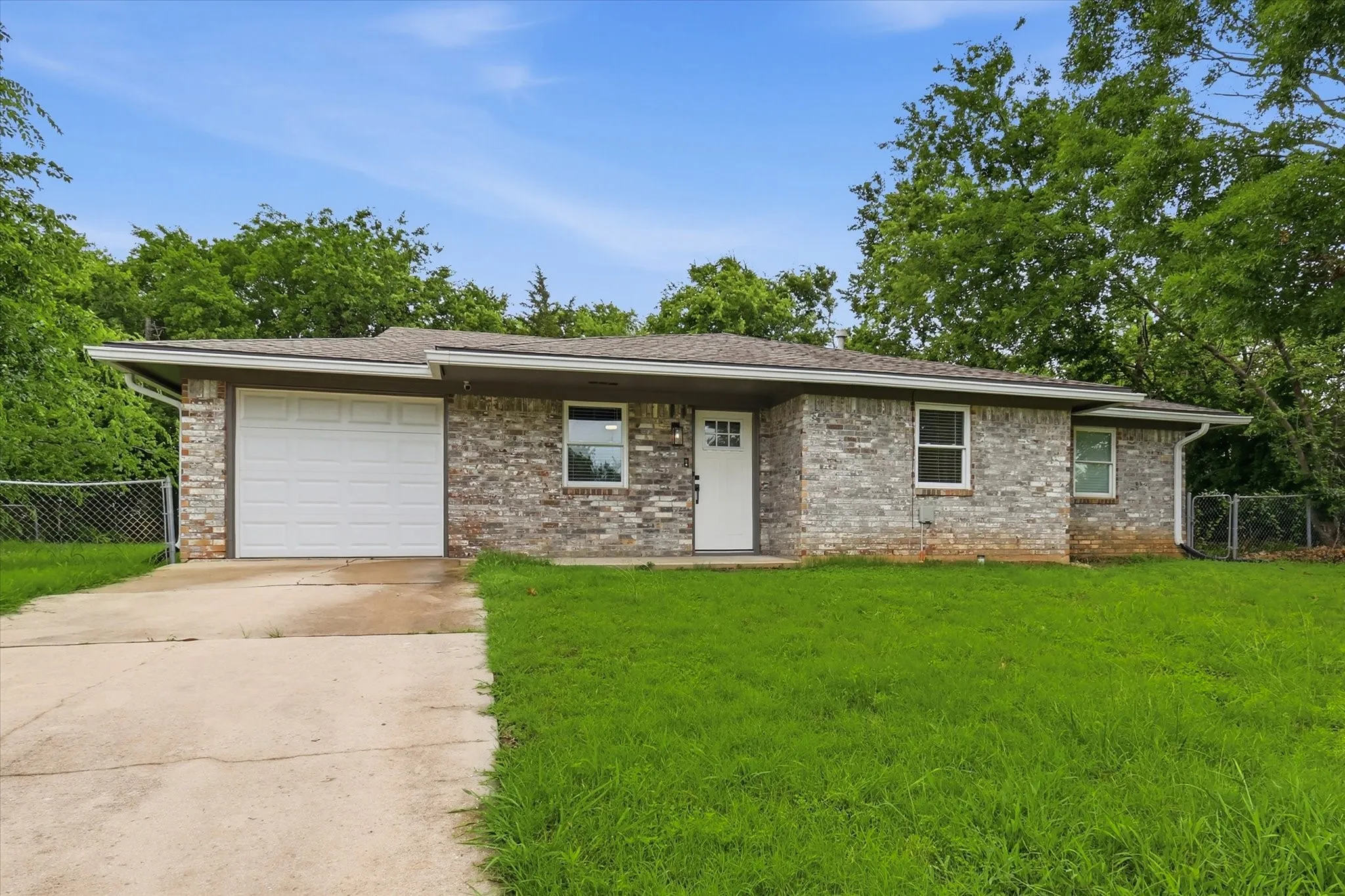 Brick exterior, attached garage, white front door, multiple windows, asphalt driveway