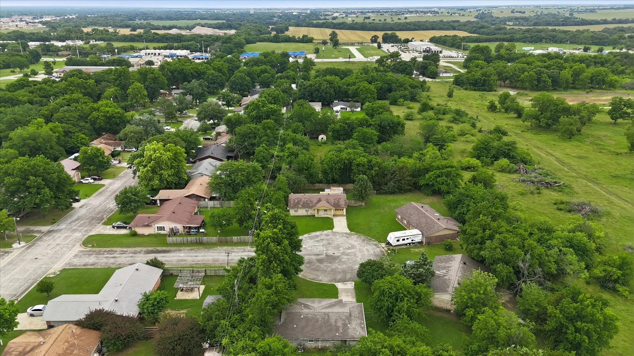 Residential properties with mature trees and green landscaping, featuring a paved cul-de-sac and surrounding undeveloped land