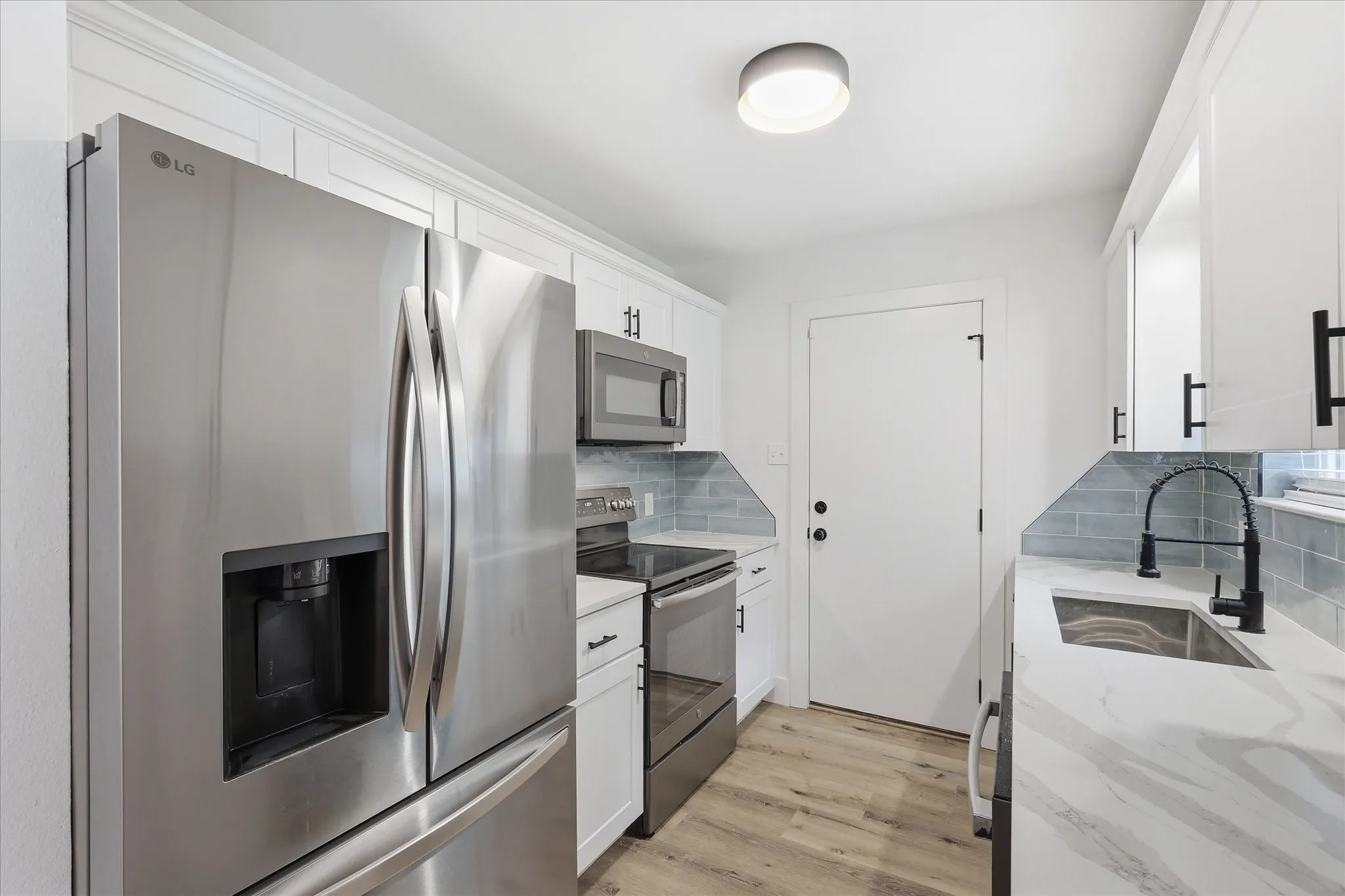 Kitchen featuring stainless steel appliances, white cabinetry, a light-toned wood-finish floor, a stainless steel sink with a black pull-down faucet, and a patterned backsplash