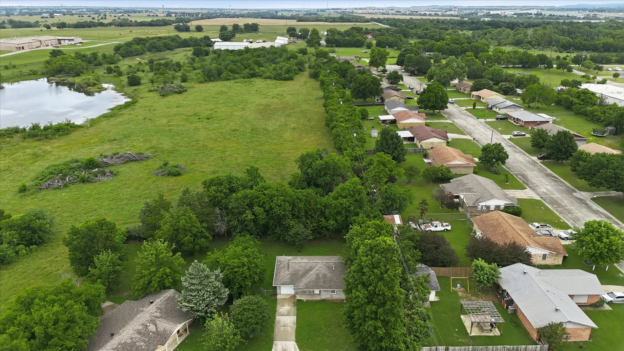 Residential street with a variety of single-story homes, mature trees, and an open green space with a pond