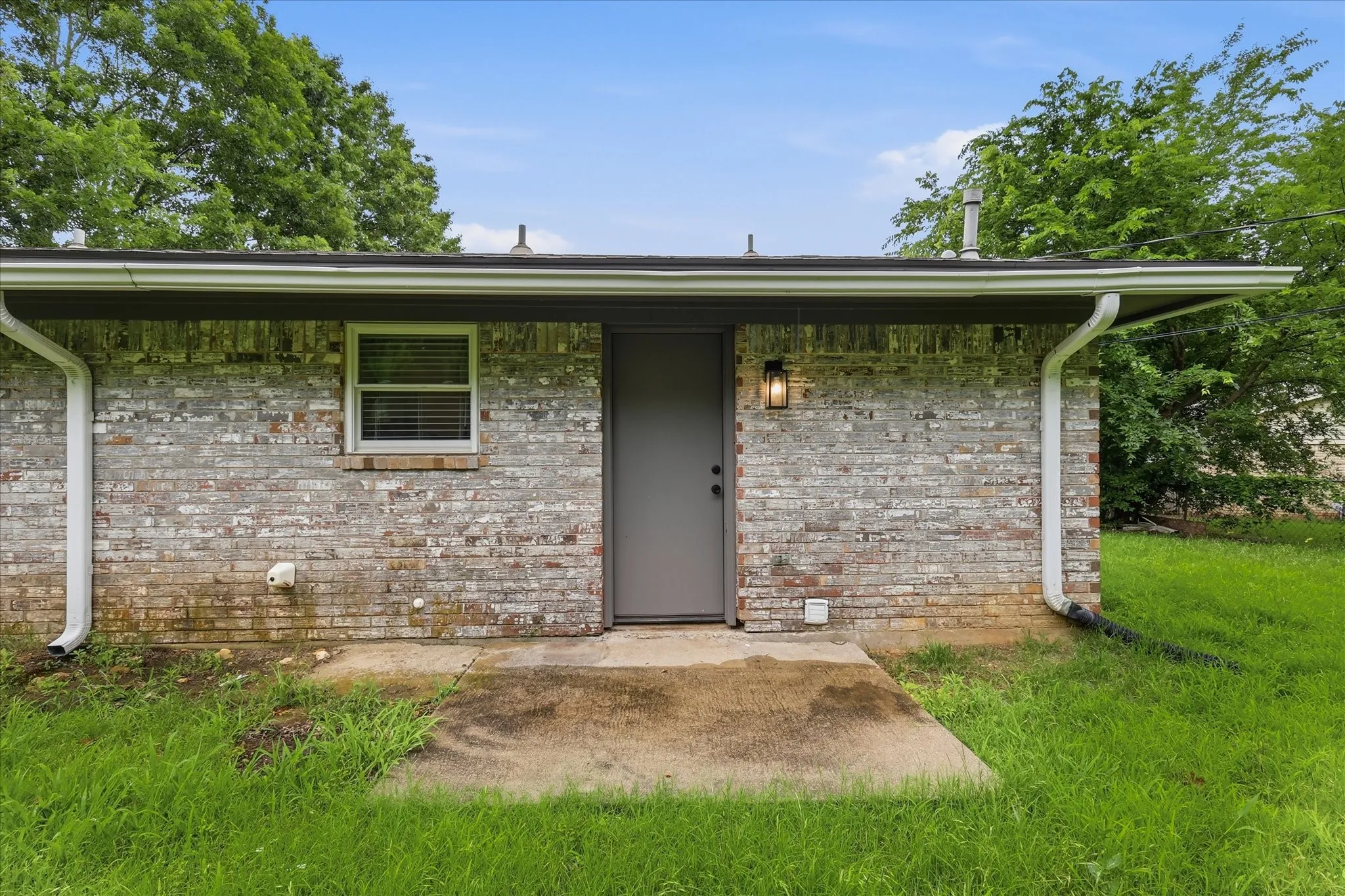 Brick exterior with a covered patio, a single entry door, and an exterior light fixture