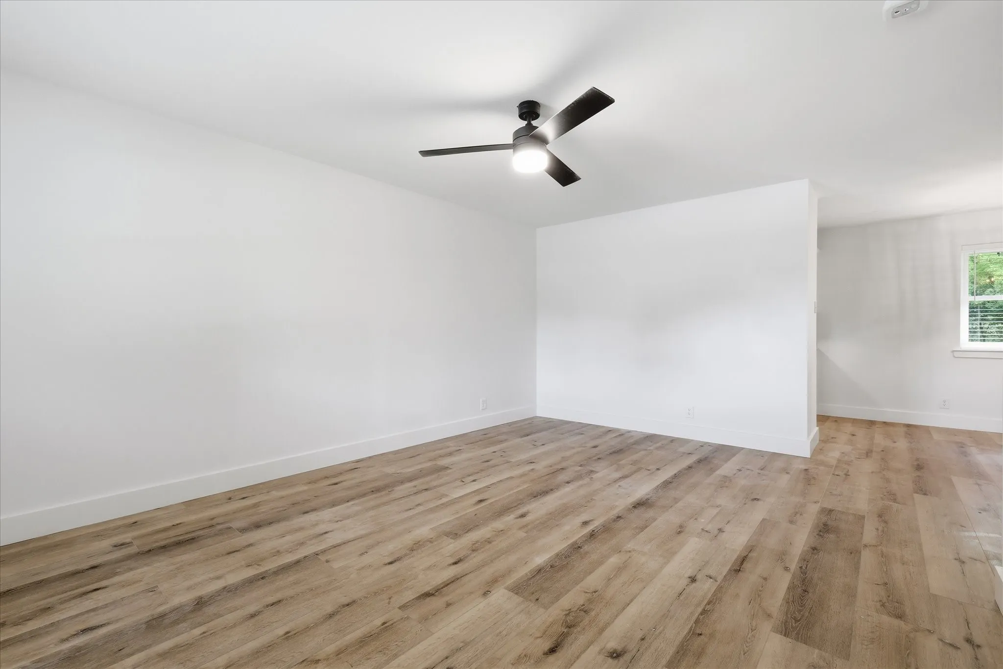 Spacious room featuring wood-finish flooring, white walls, and a modern ceiling fan with integrated lighting