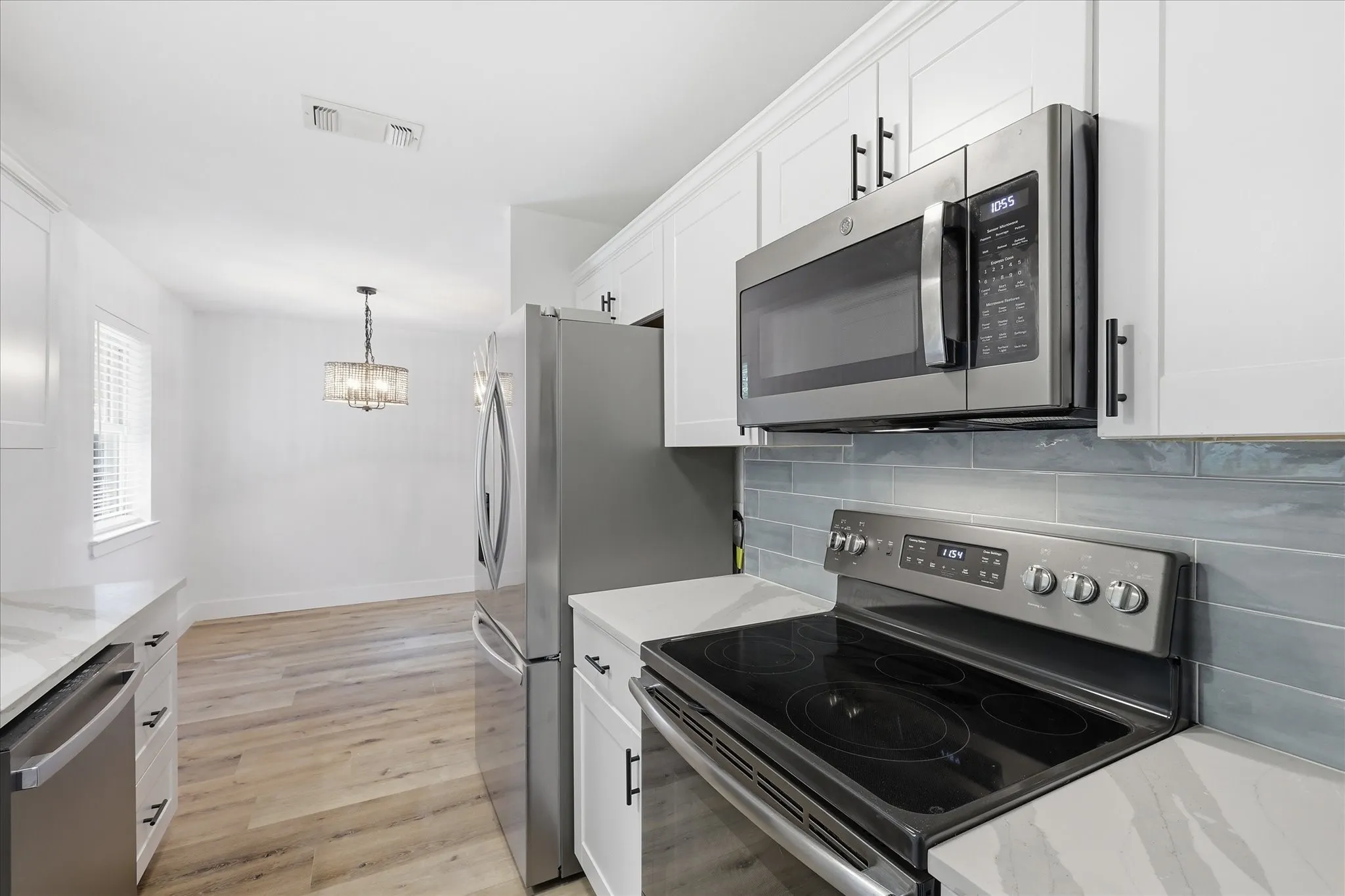 Kitchen featuring stainless steel appliances, white cabinetry with dark hardware, a tile backsplash, and light-toned countertops
