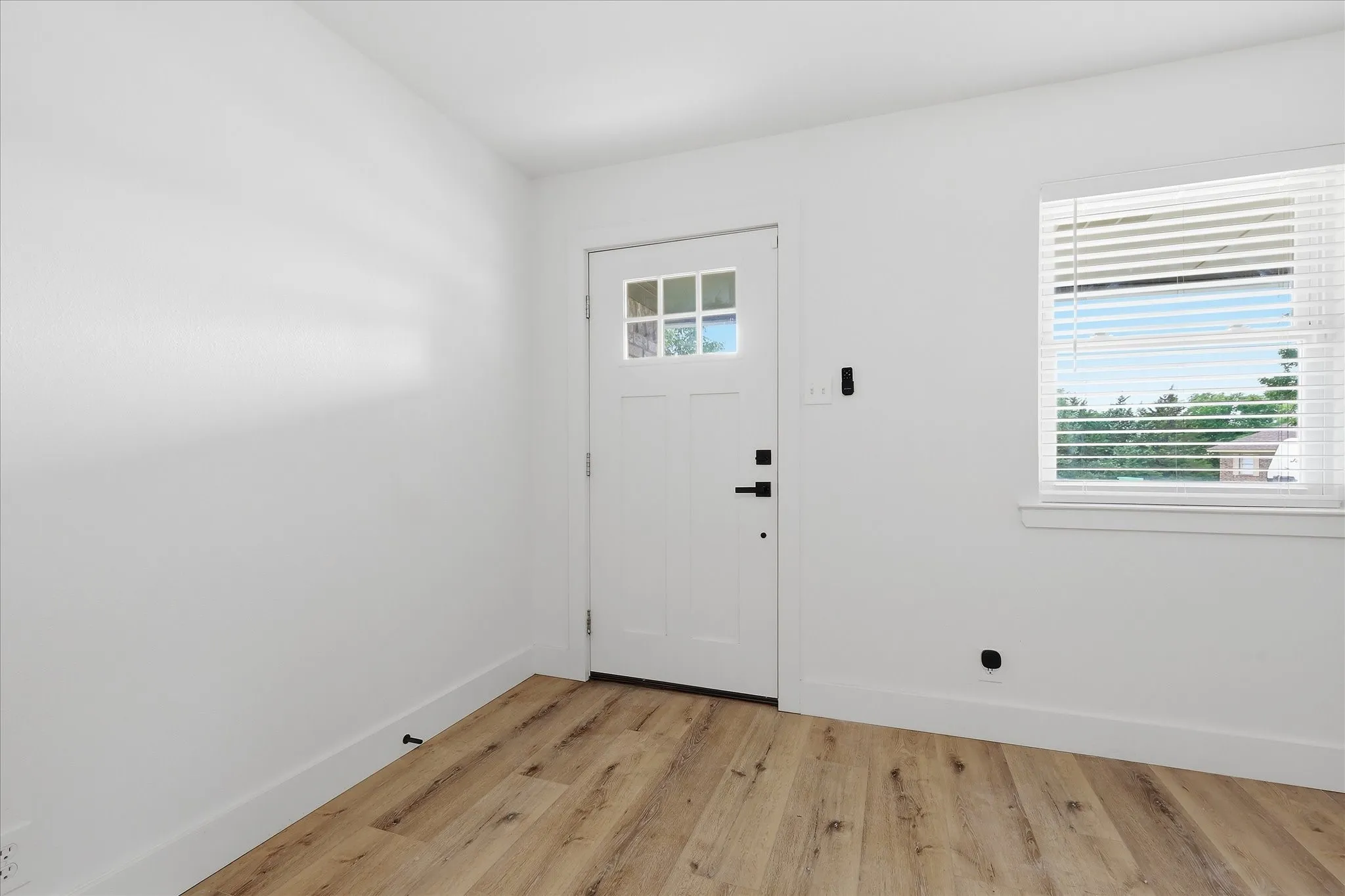 Entryway featuring wood-finish flooring, white walls, a window with blinds, and a door with frosted glass panes