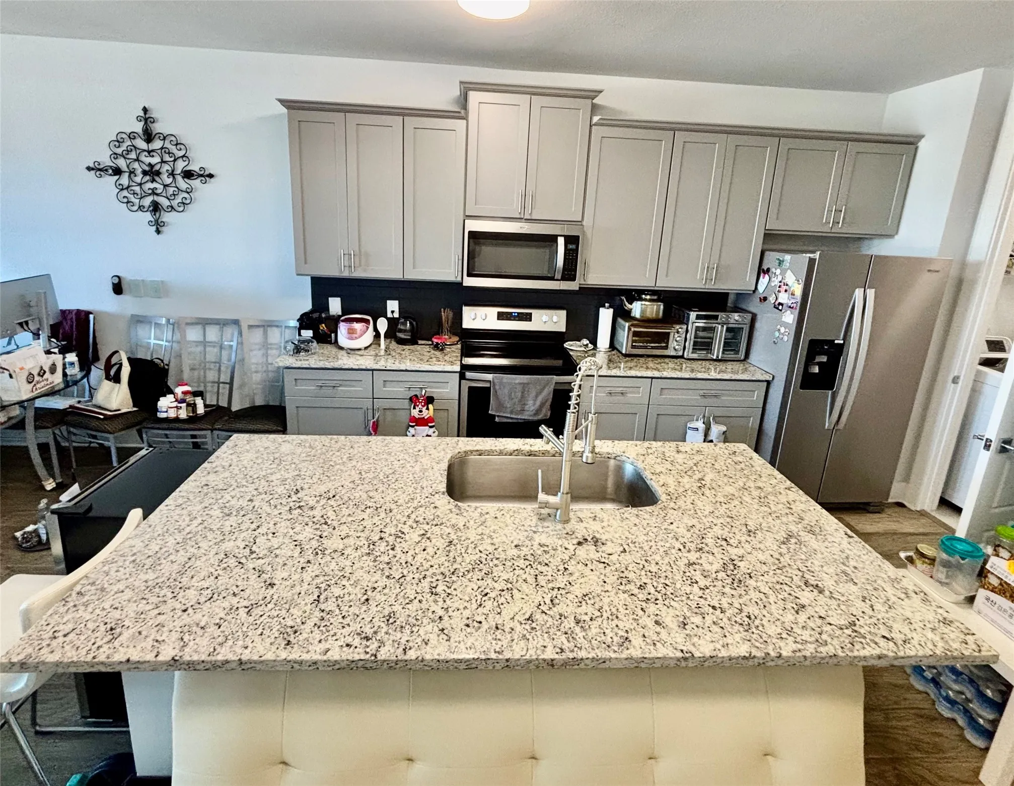Kitchen island with an undermount sink, a gooseneck faucet, light-toned cabinetry, light-toned countertops, and stainless steel appliances