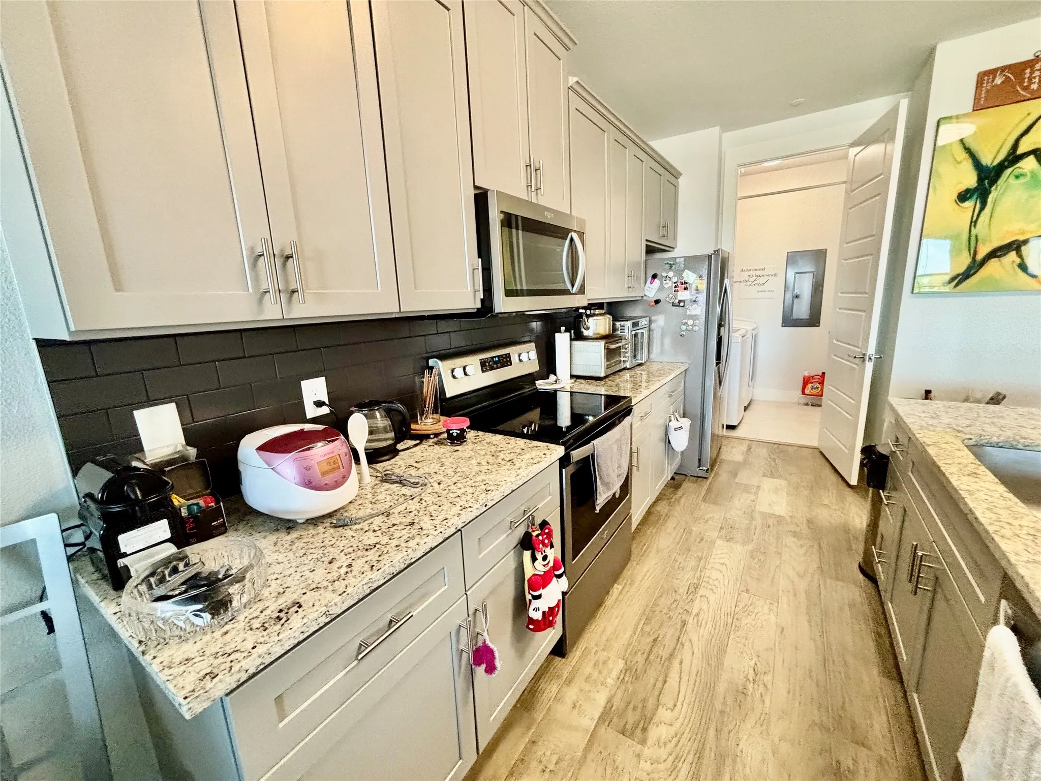 Kitchen featuring light-toned cabinetry, granite-finish countertops, stainless steel appliances, a dark subway tile backsplash, and wood-finish flooring