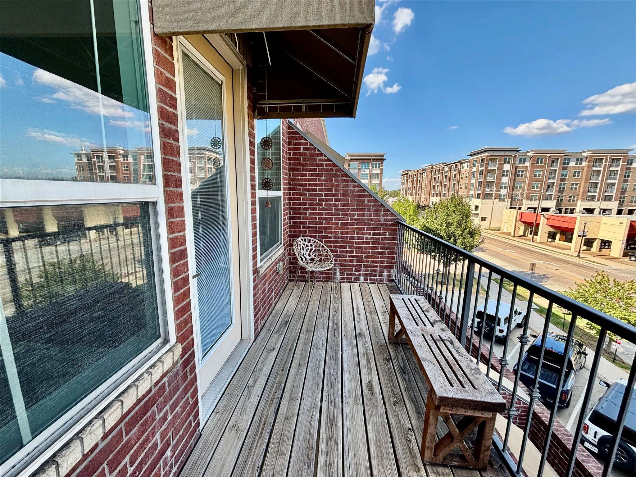Outdoor balcony with wood-finish decking, black metal railing, and a red brick exterior
