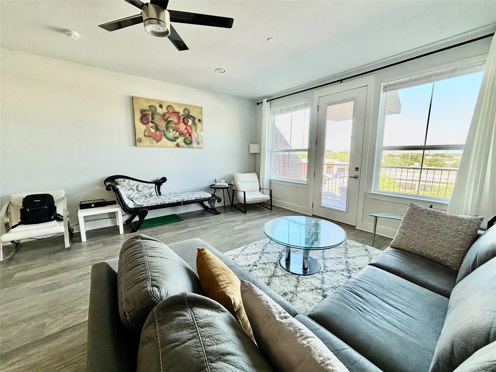 Bright living area featuring wood-finish flooring, a ceiling fan, and large windows with a glass-paneled door