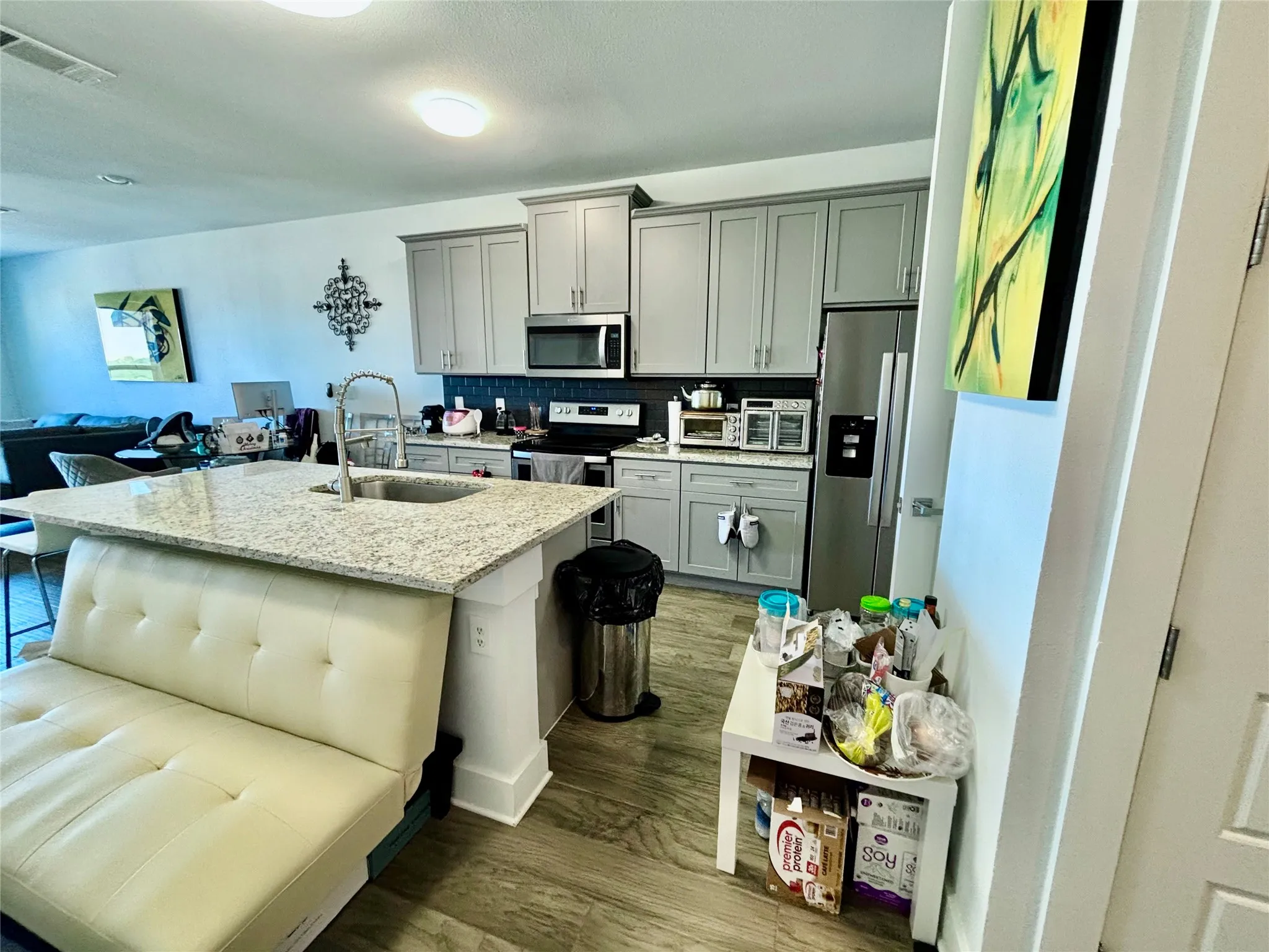 Kitchen featuring light gray cabinetry, stainless steel appliances, a large island with an integrated sink, and wood-finish flooring