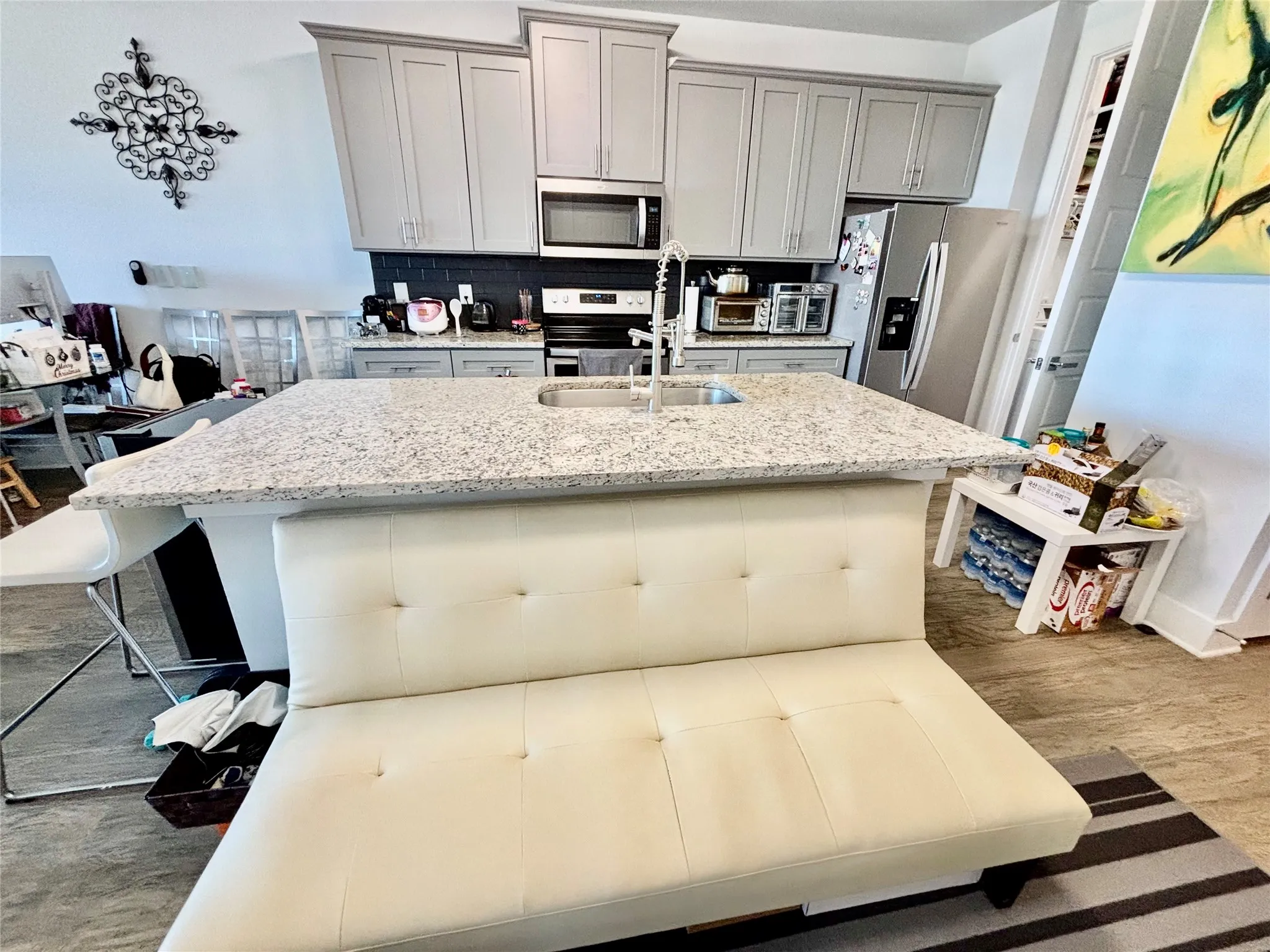Kitchen featuring light gray cabinetry, stainless steel appliances, a dark subway tile backsplash, a large island with a sink, and granite countertops
