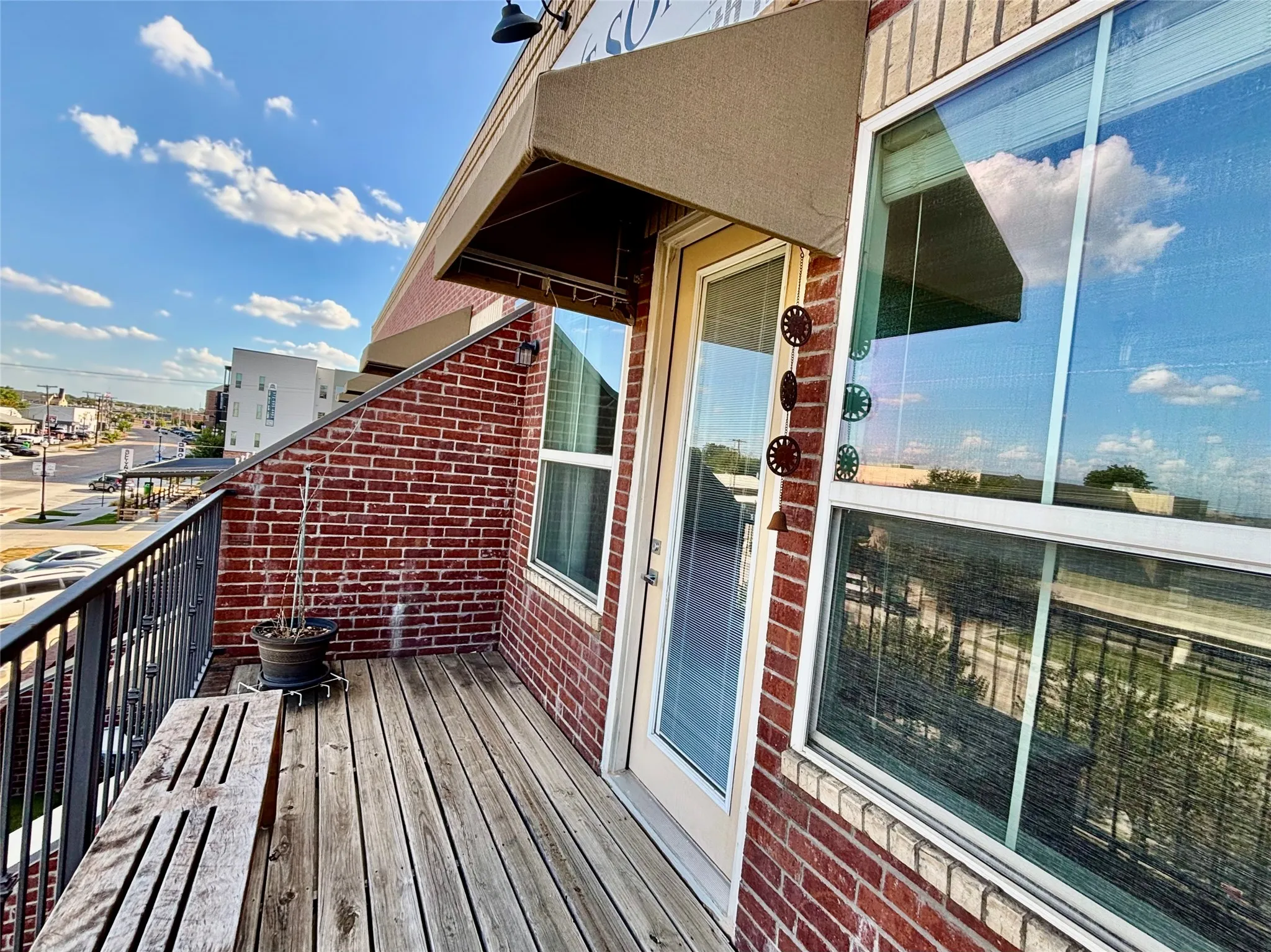 Balcony featuring wood-finish decking, brick exterior wall, and metal railing
