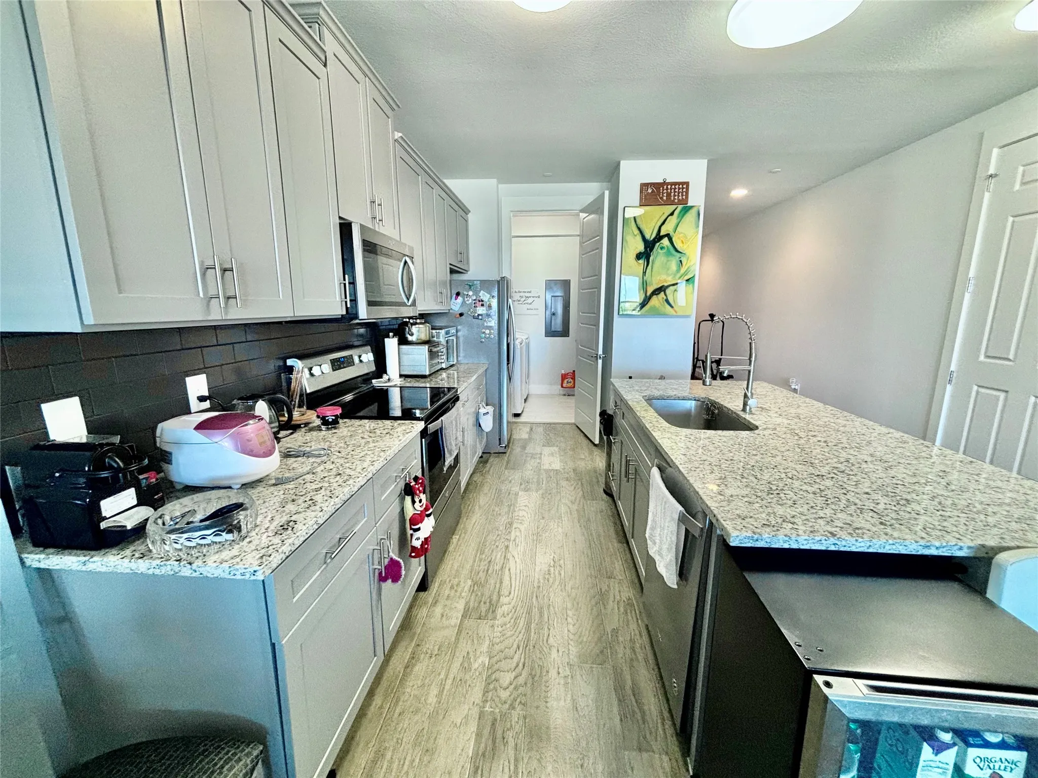 Galley kitchen featuring light gray cabinetry, light speckled countertops, stainless steel appliances, a dark subway tile backsplash, and wood-finish flooring