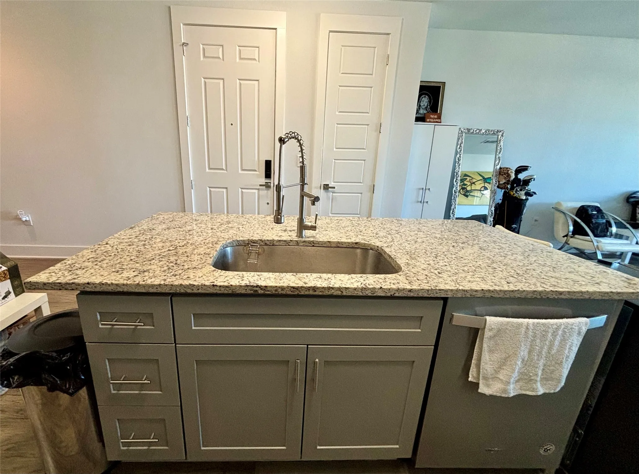 Kitchen island with a stainless-steel sink, gooseneck faucet, light-colored granite countertop, gray cabinetry, and an integrated dishwasher
