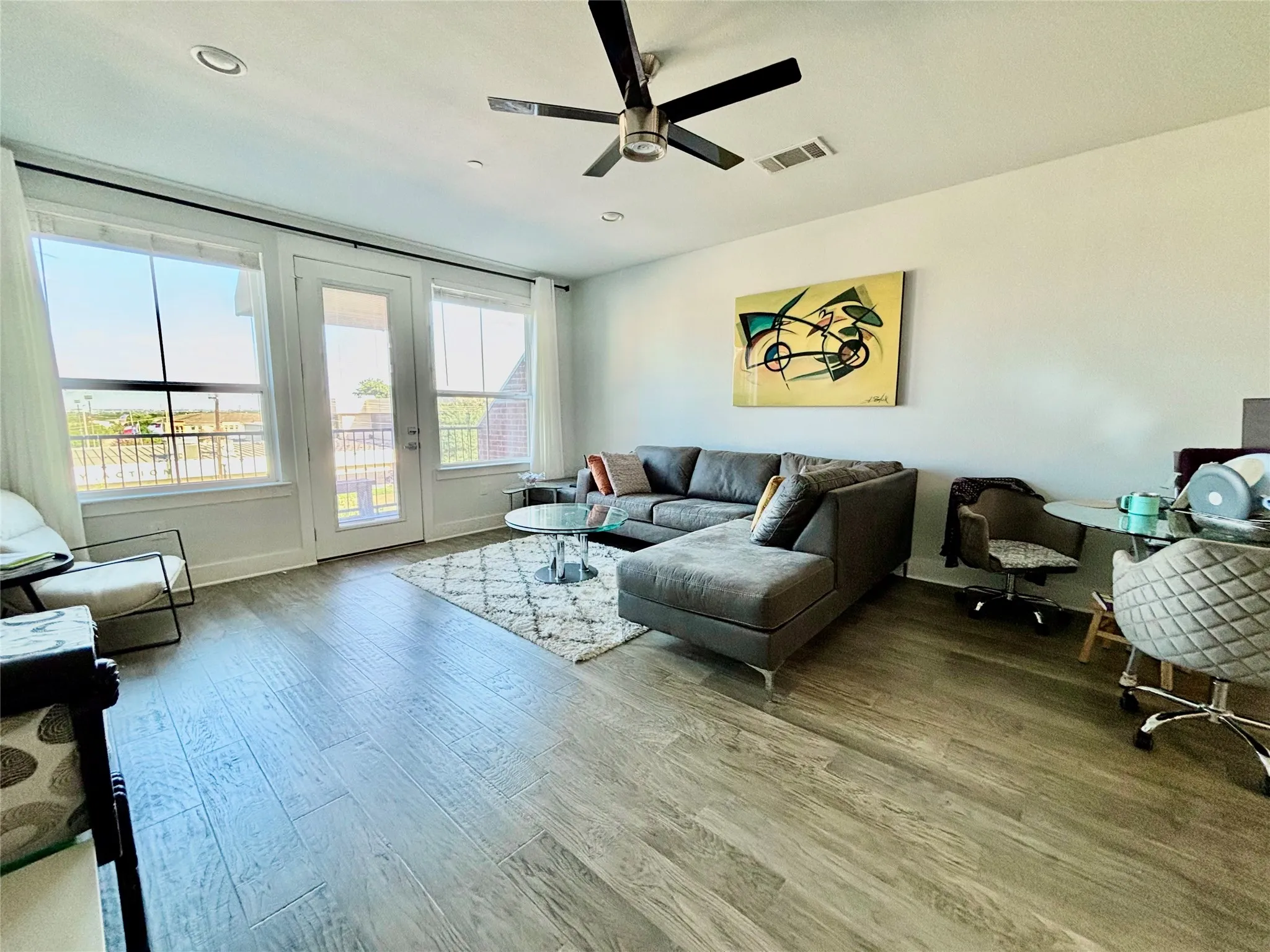 Wood-finish flooring throughout, ceiling fan with integrated lighting, recessed lighting, and a glass-paneled door opening to an outdoor area