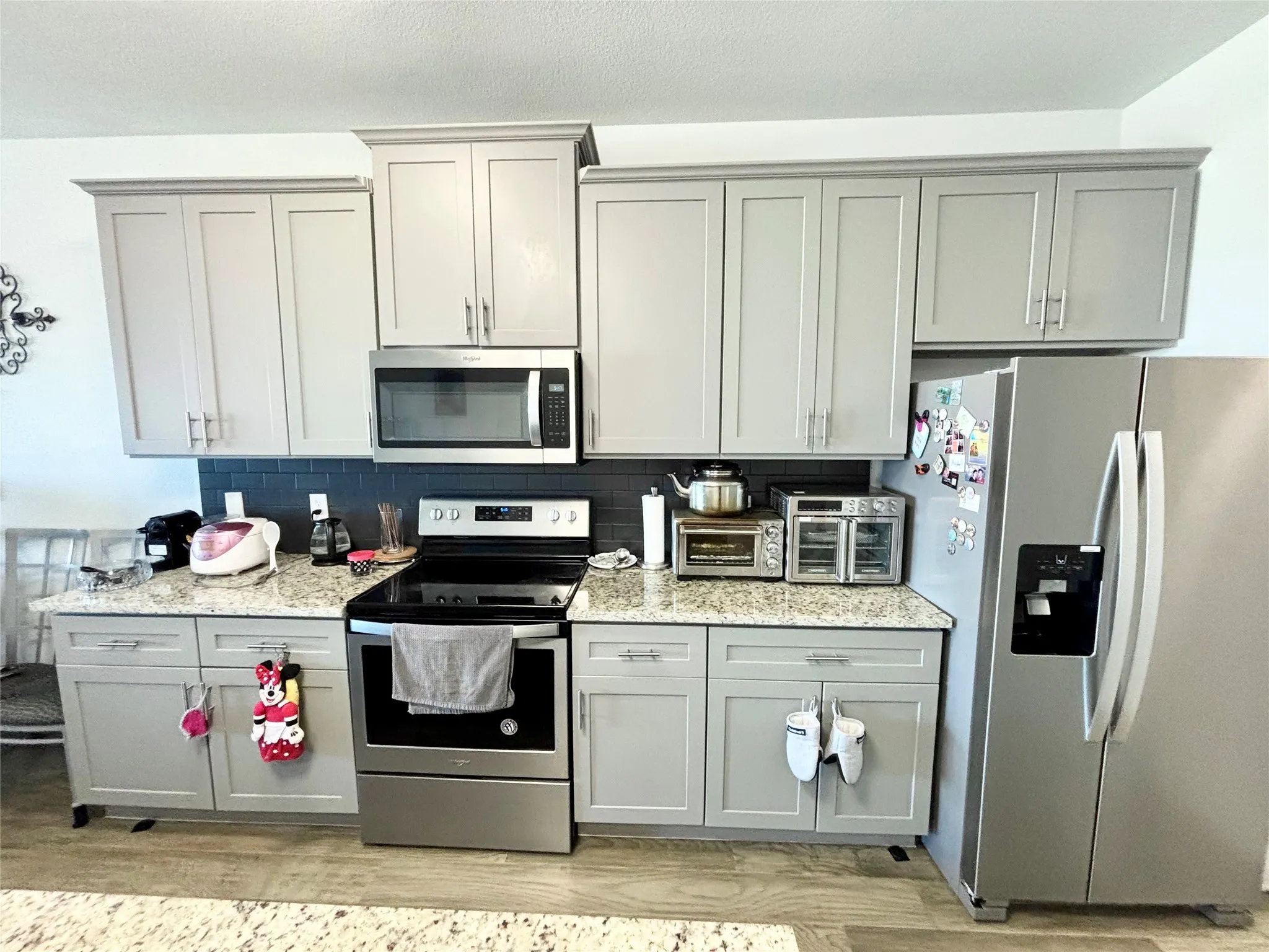 Stainless steel appliances, light-toned cabinetry, dark subway tile backsplash, light speckled countertops, and wood-finish flooring