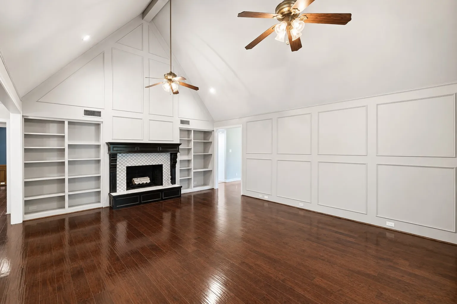 Vaulted ceiling with wood-finish flooring, featuring a fireplace with tile surround, built-in shelving, and decorative wall paneling