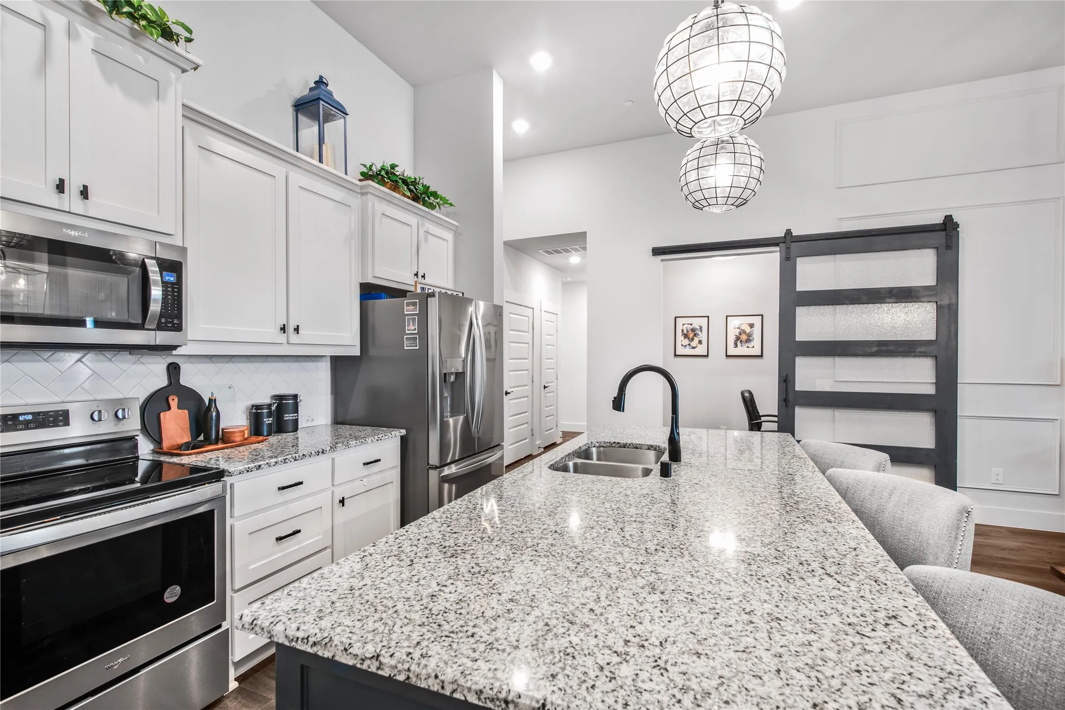 Kitchen featuring stainless steel appliances, white cabinetry, a tile backsplash, a large island with a double basin sink, and pendant lighting
