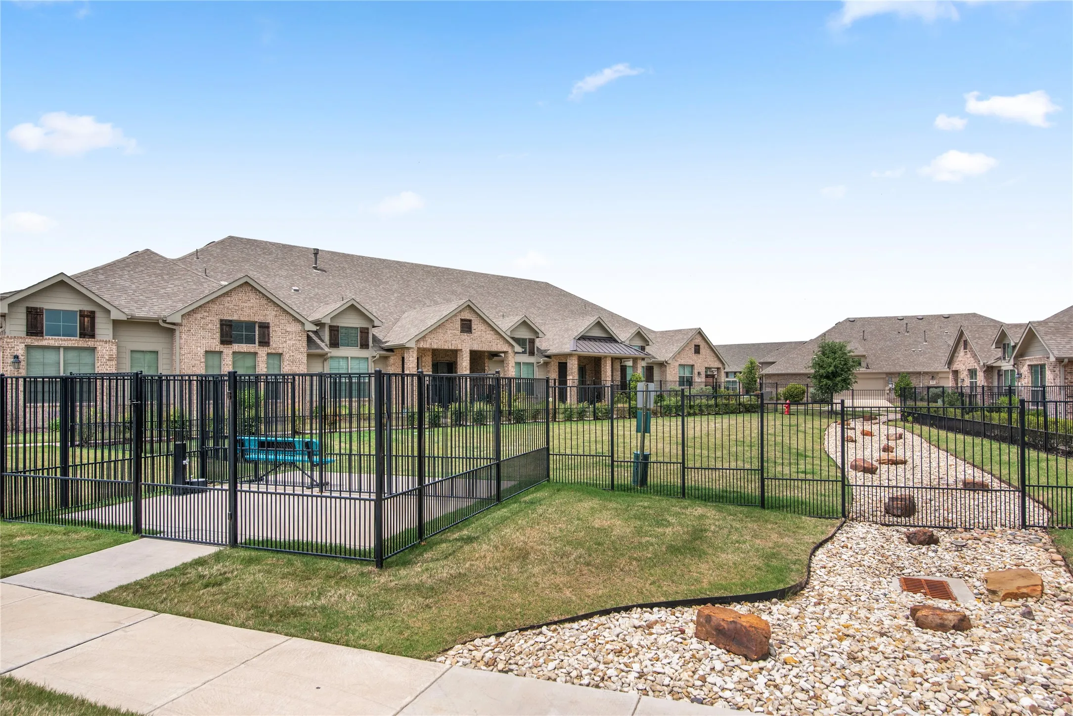 Fenced outdoor area with a gravel path, grass sections, and scattered large rocks