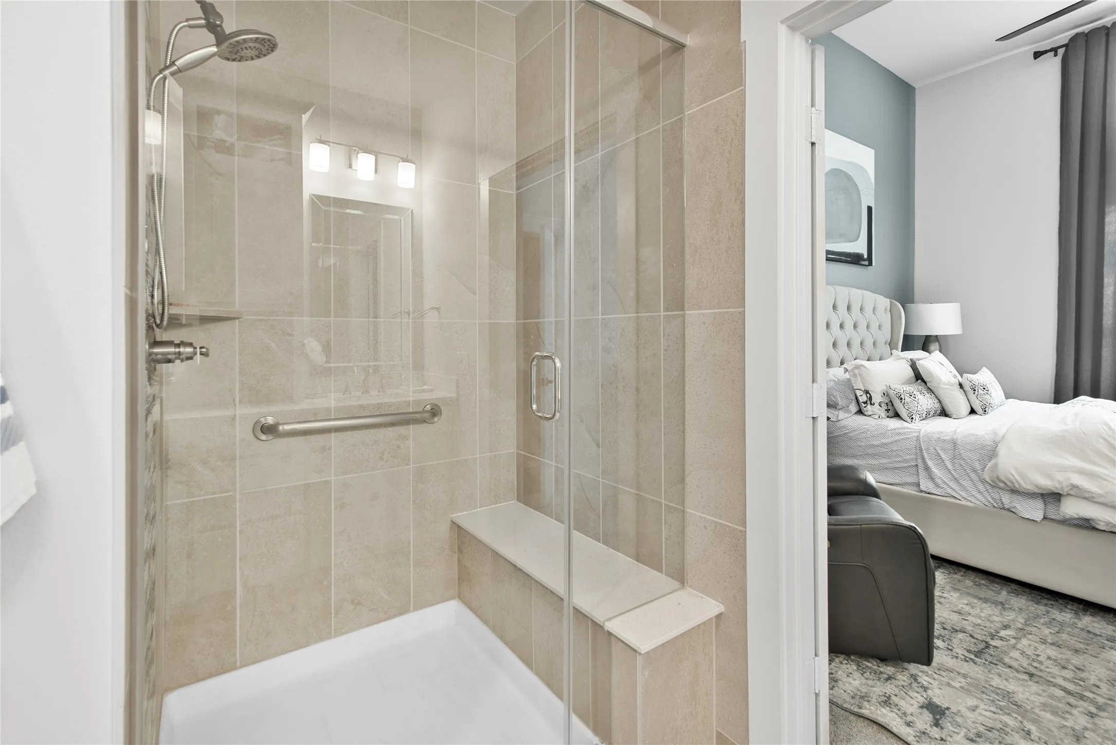 Glass-enclosed shower with full tile surround, built-in bench, handheld shower fixture, and grab bar