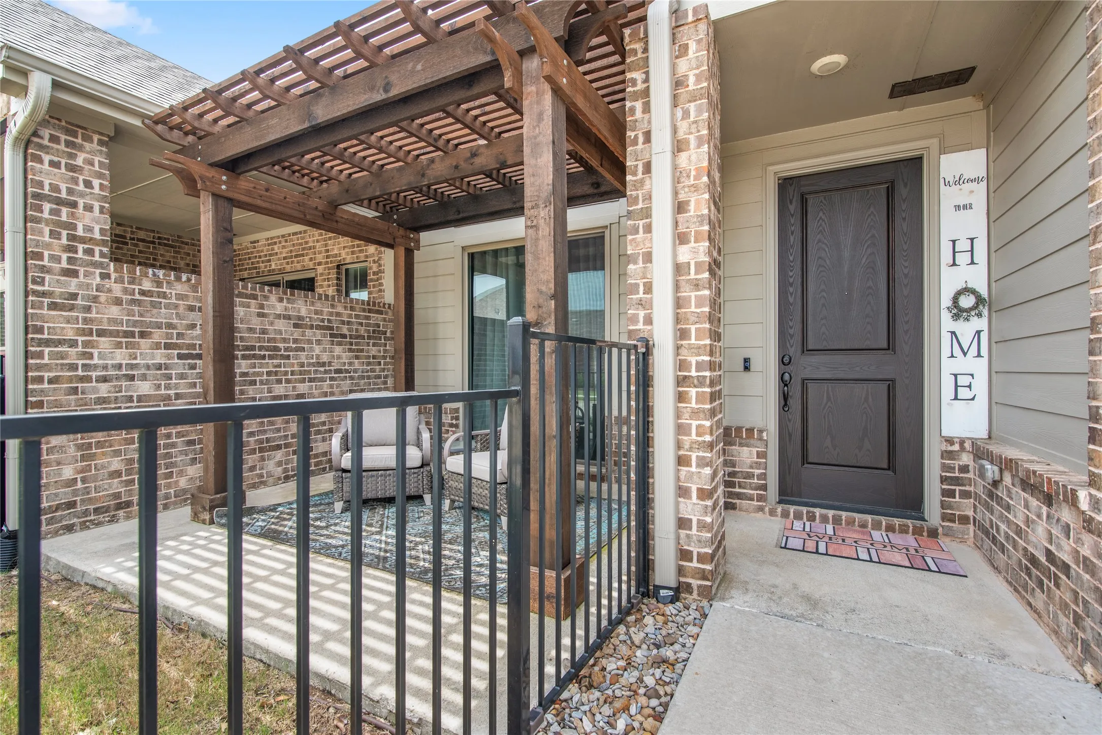 Covered patio with a wood pergola, brick accent walls, and a dark-paneled entry door
