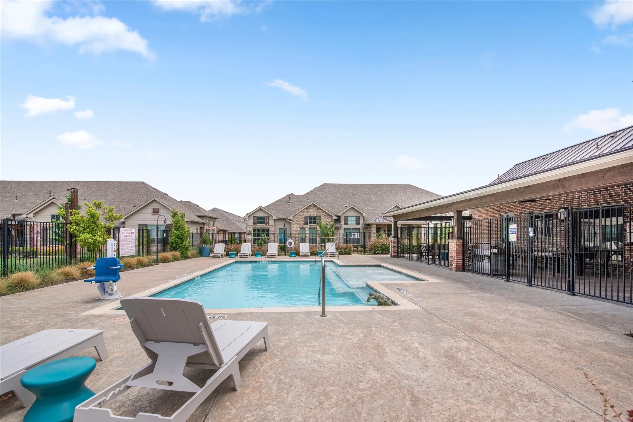 Community pool with an integrated spa, surrounded by a concrete patio and a covered outdoor area