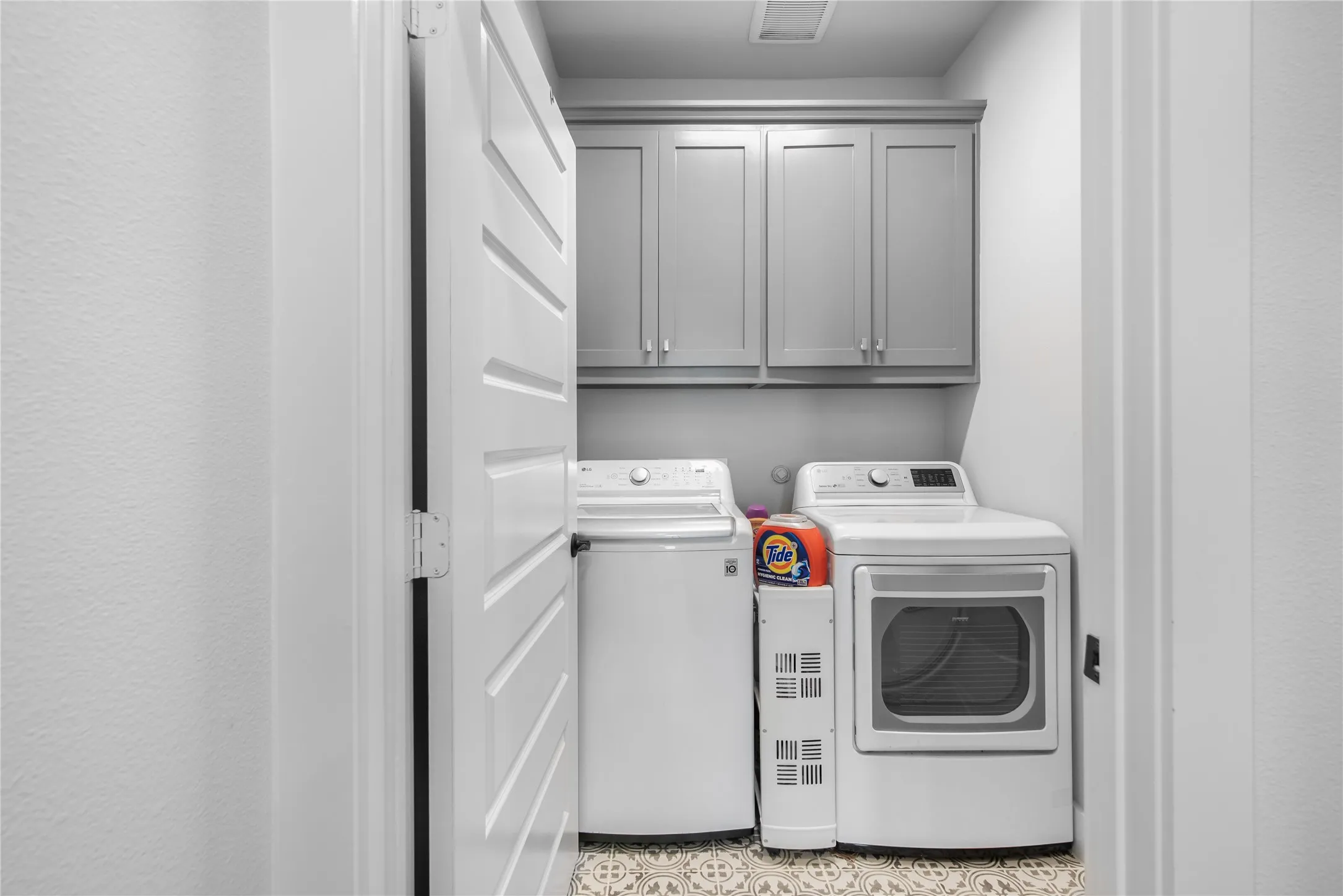 Laundry area featuring gray shaker cabinetry, patterned floor tiles, and a white paneled door