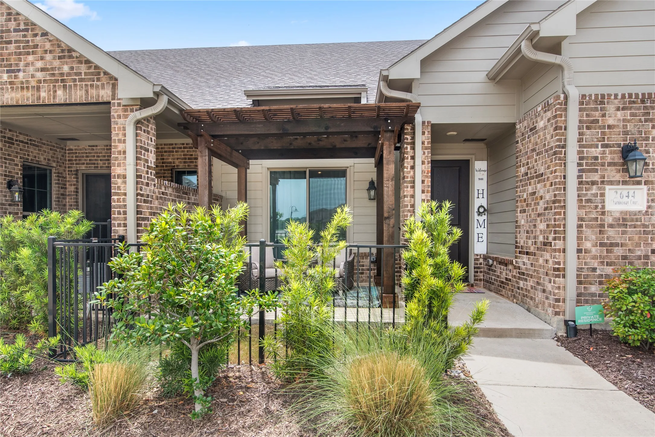 Brick exterior with siding accents, covered entry, front patio with a wood pergola, and mature landscaping