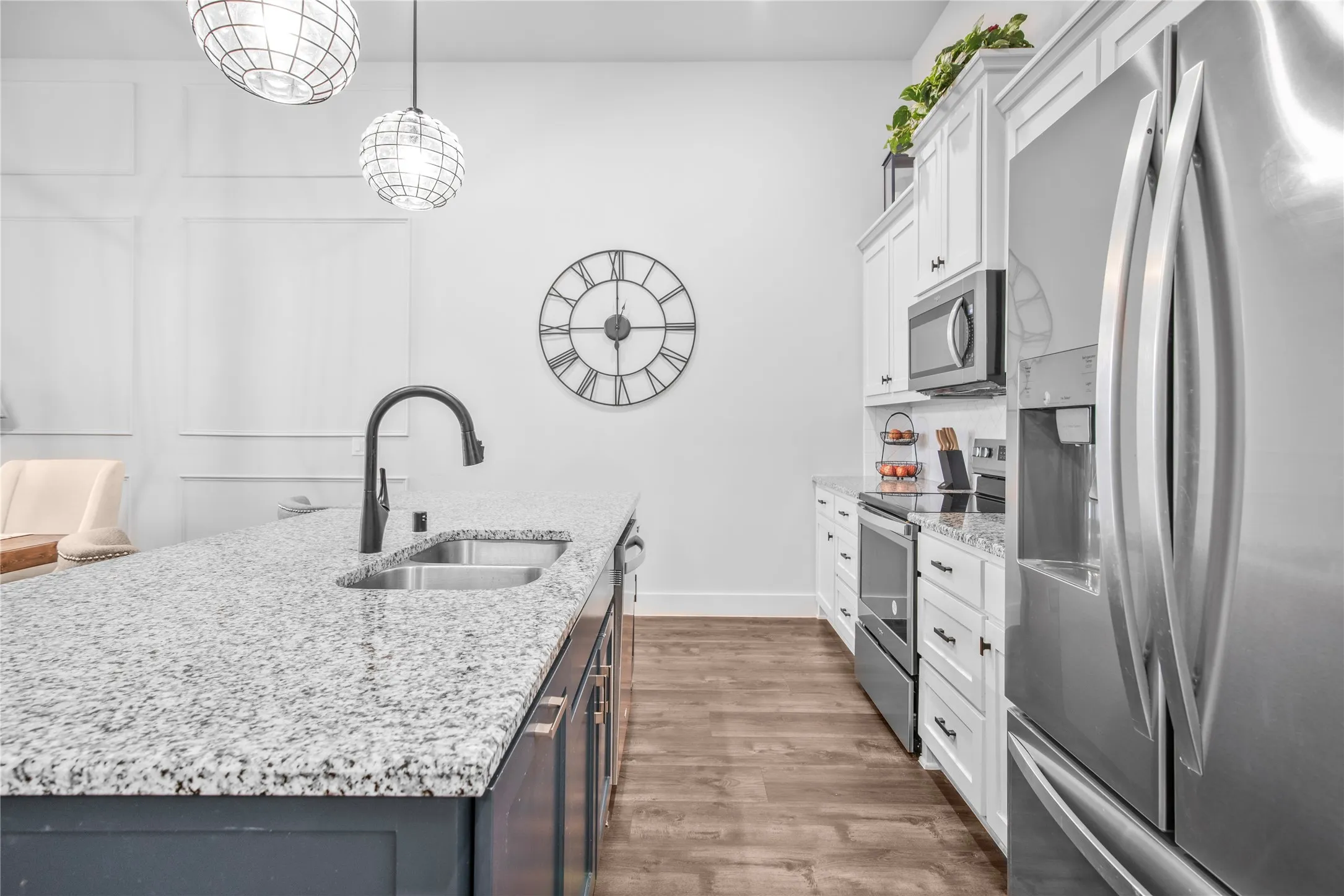 Kitchen featuring stainless steel appliances, granite countertops, wood-finish flooring, white upper cabinetry, and a central island with a sink and matte black faucet