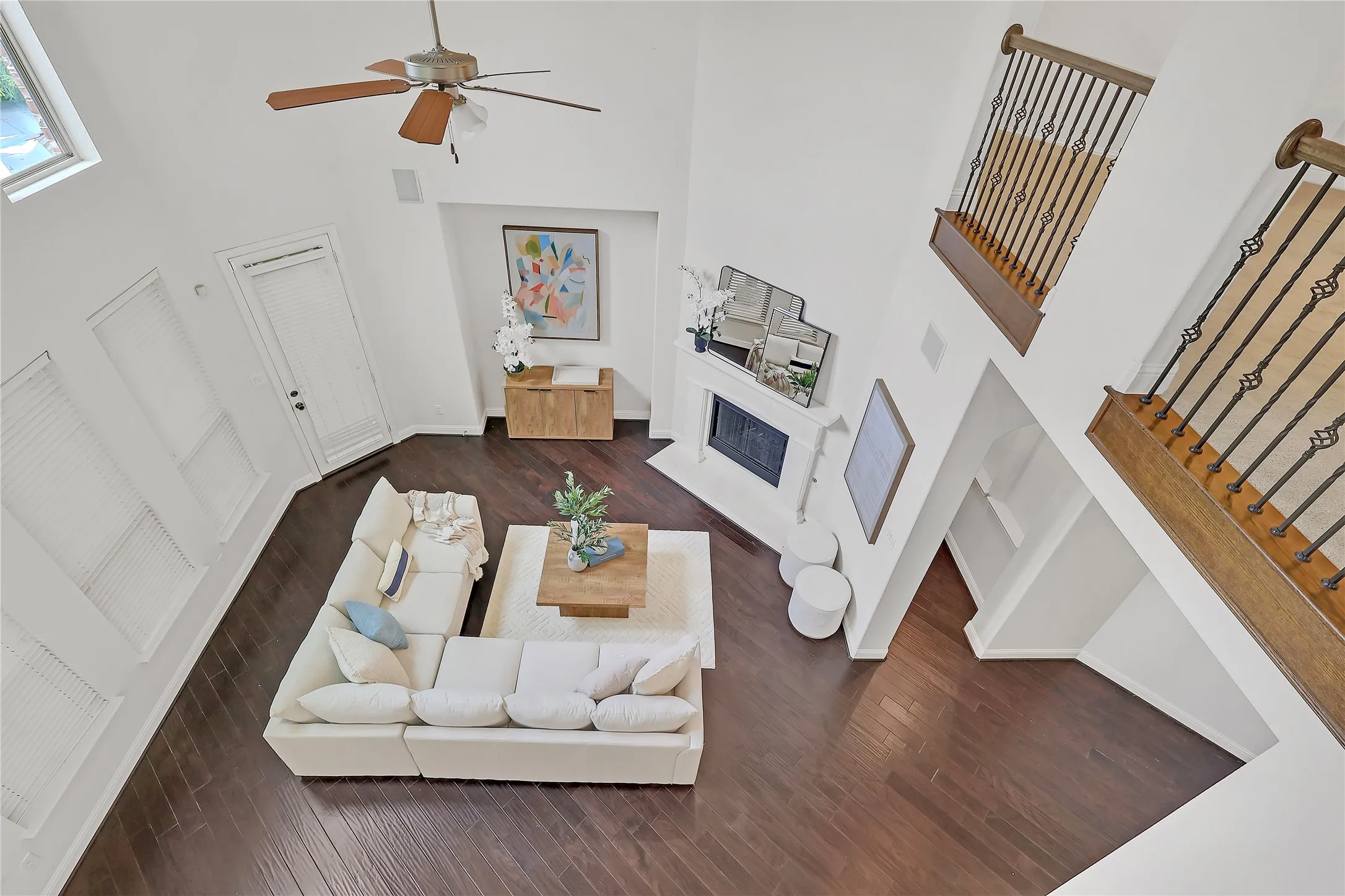 Living room featuring a towering ceiling, wood finished floors, a fireplace, stairs, and ceiling fan