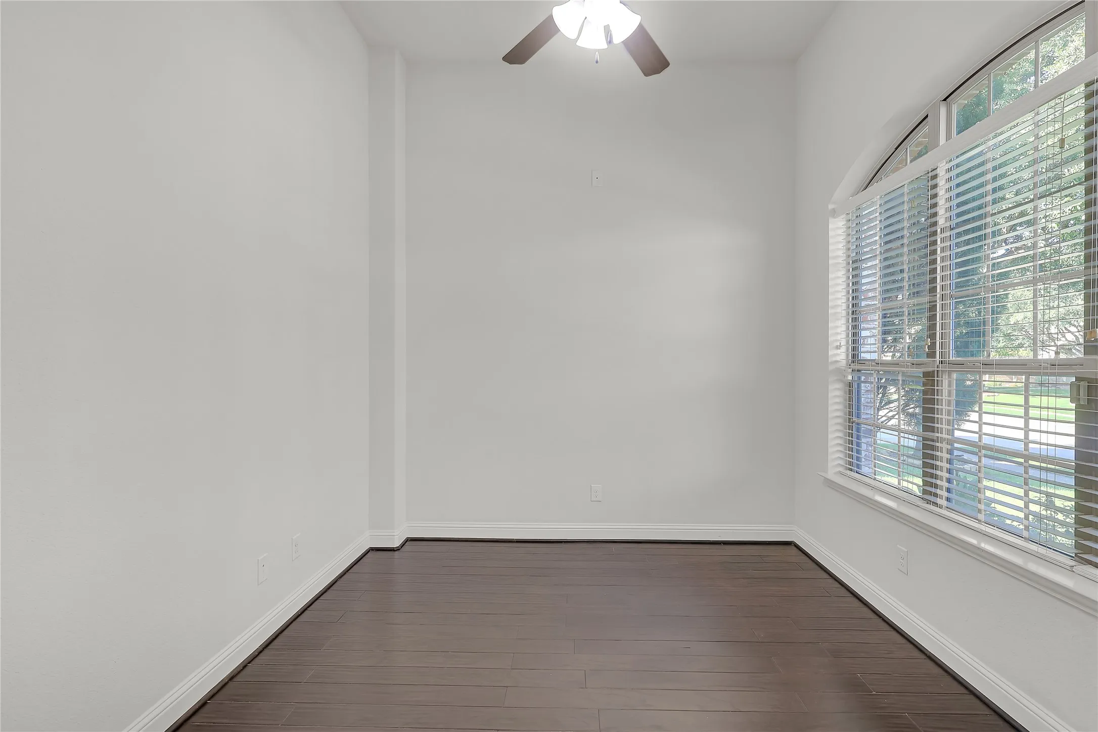 Empty room with dark wood-style floors and a ceiling fan