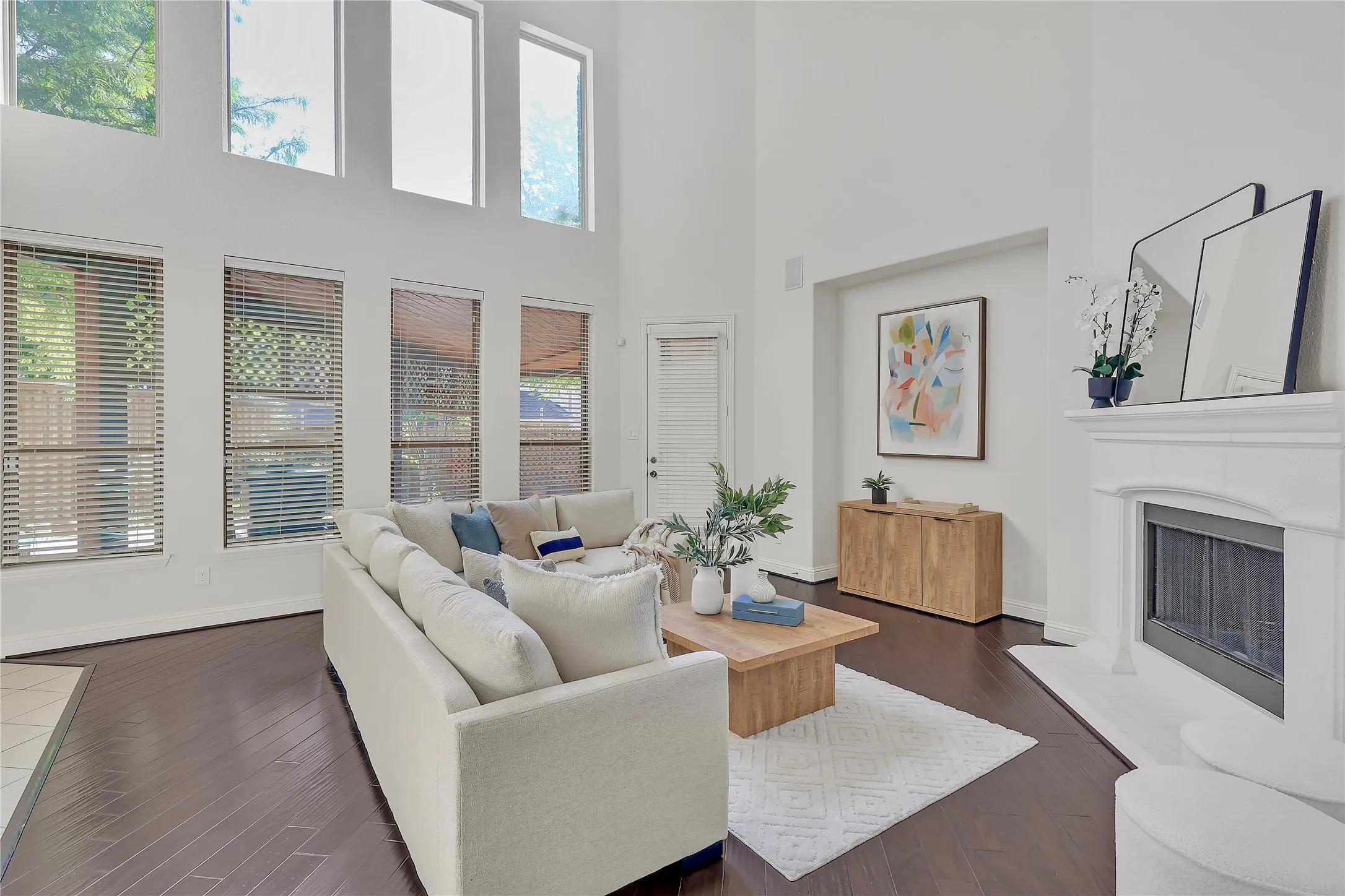 Living room with plenty of natural light, a towering ceiling, dark wood-style floors, and a fireplace with raised hearth