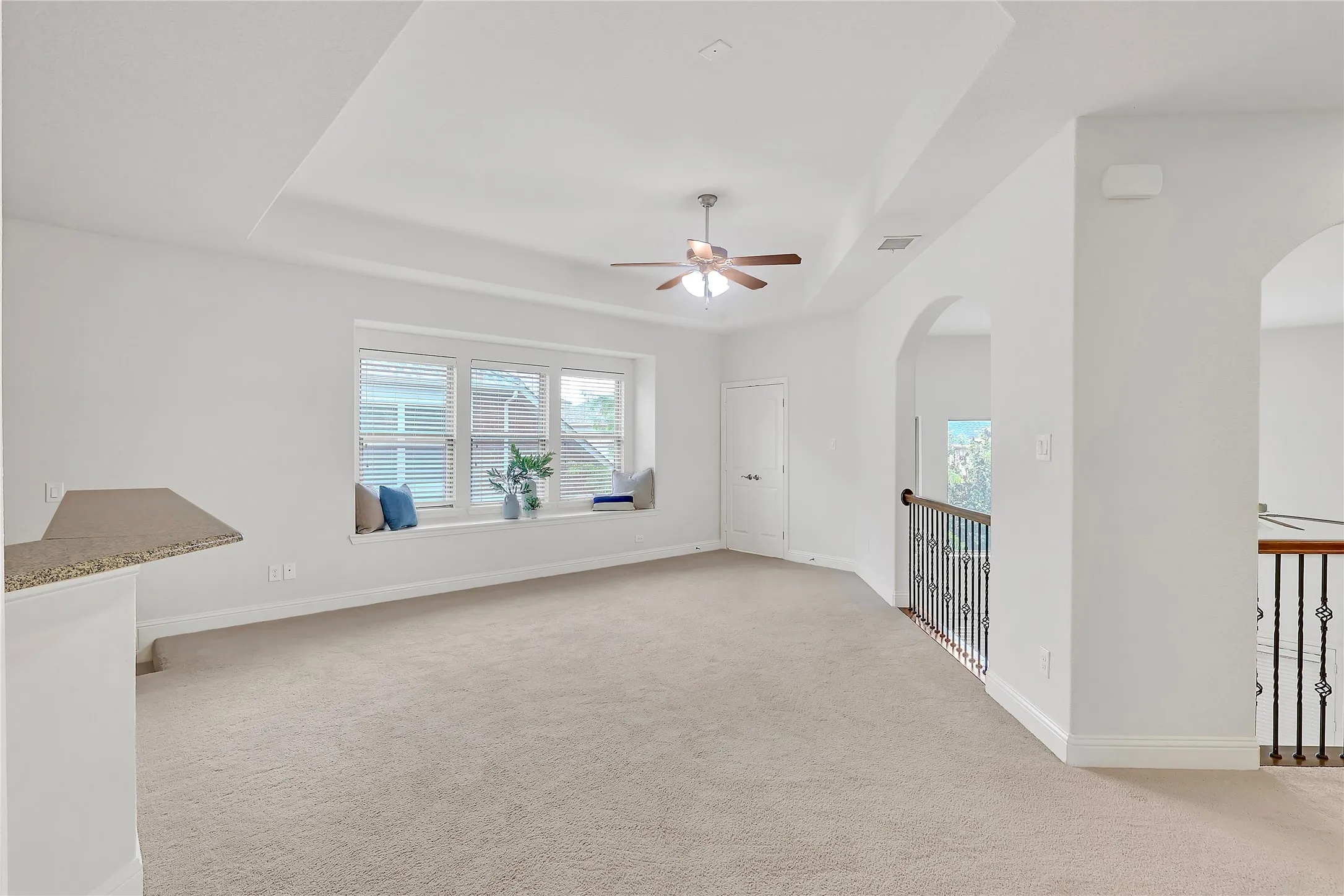 Empty room featuring arched walkways, a raised ceiling, a ceiling fan, and carpet flooring