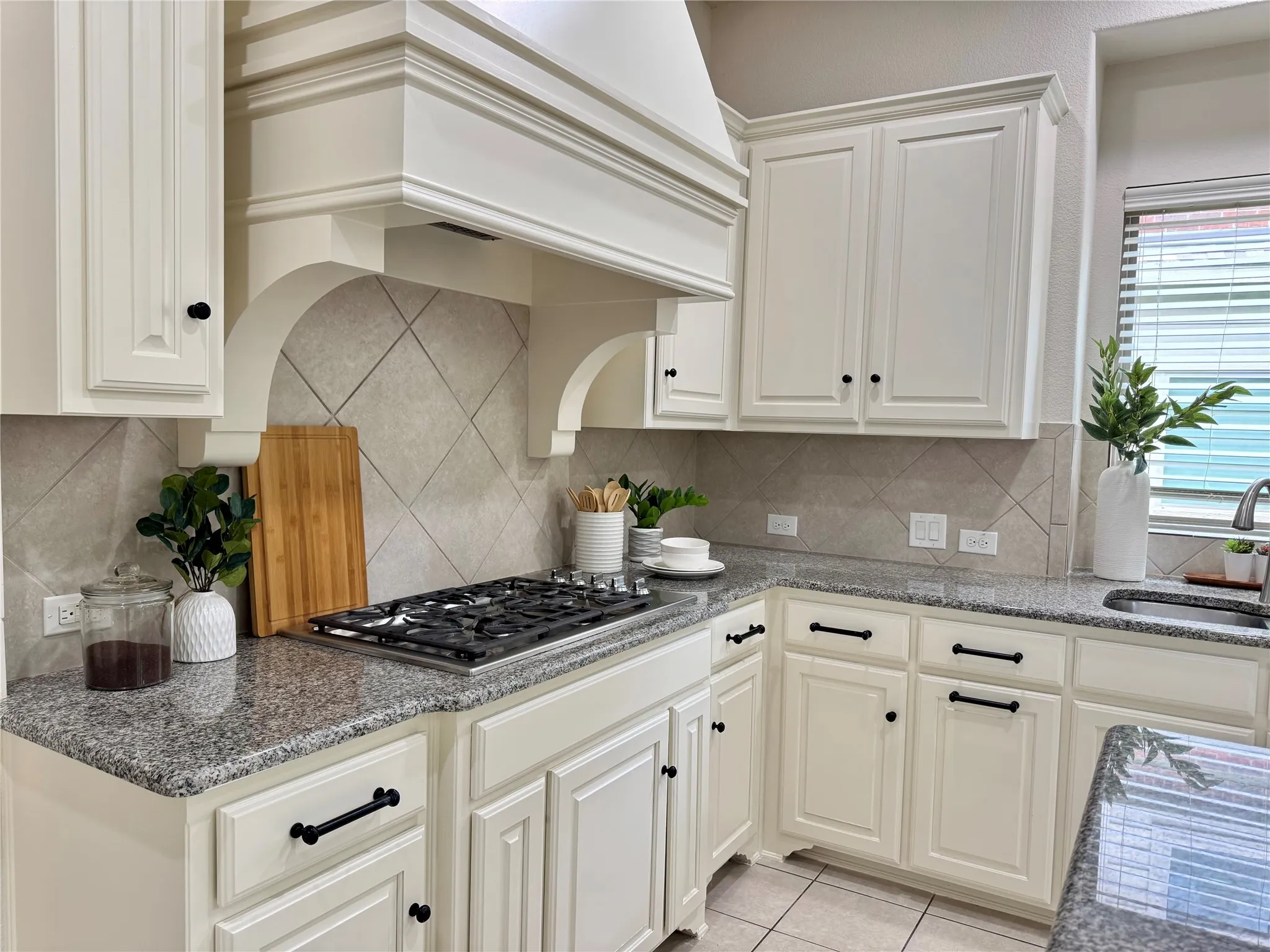 Kitchen with stainless steel gas cooktop, custom range hood, tasteful backsplash, and light tile patterned floors