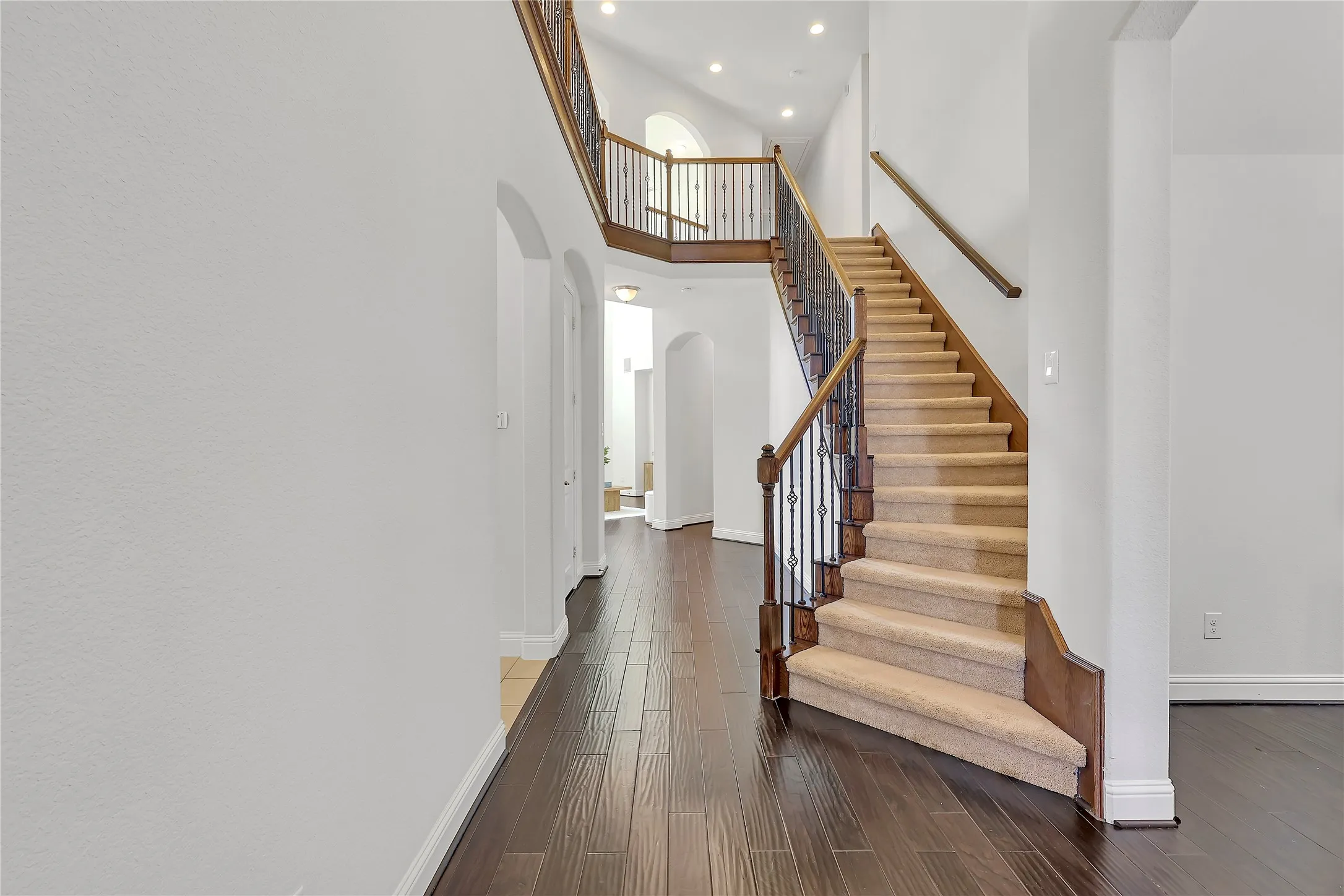 Stairway featuring arched walkways, a high ceiling, recessed lighting, and wood finished floors