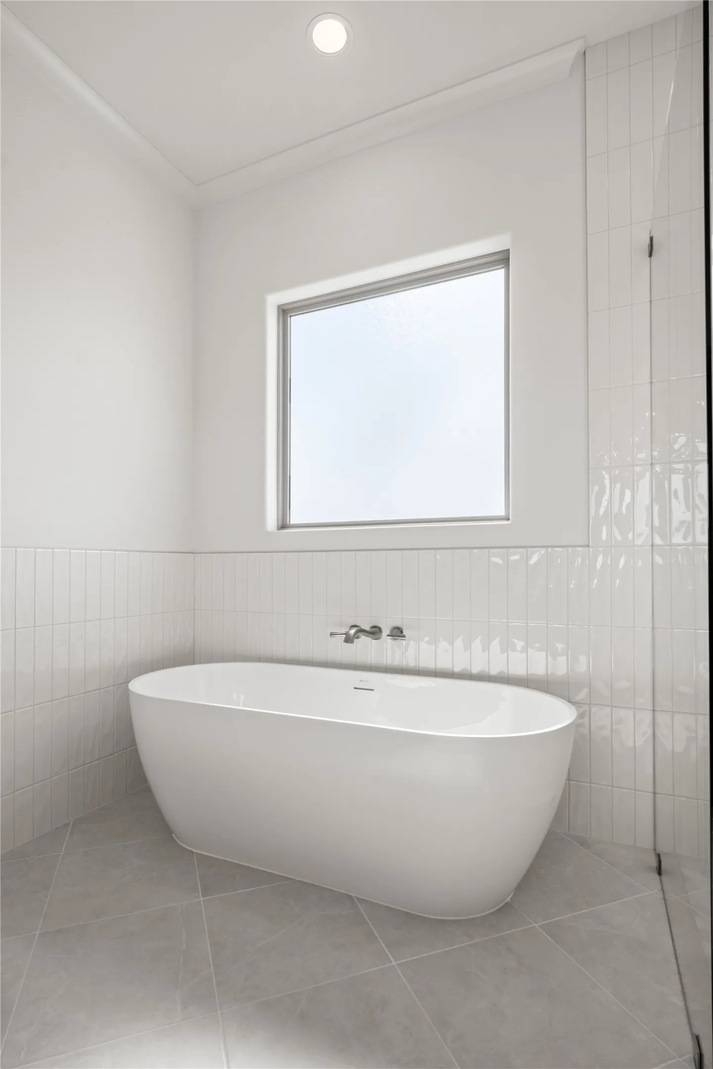 Freestanding soaking tub with wall-mounted fixtures, large window, vertical subway tile accents, recessed lighting, and large format floor tiles