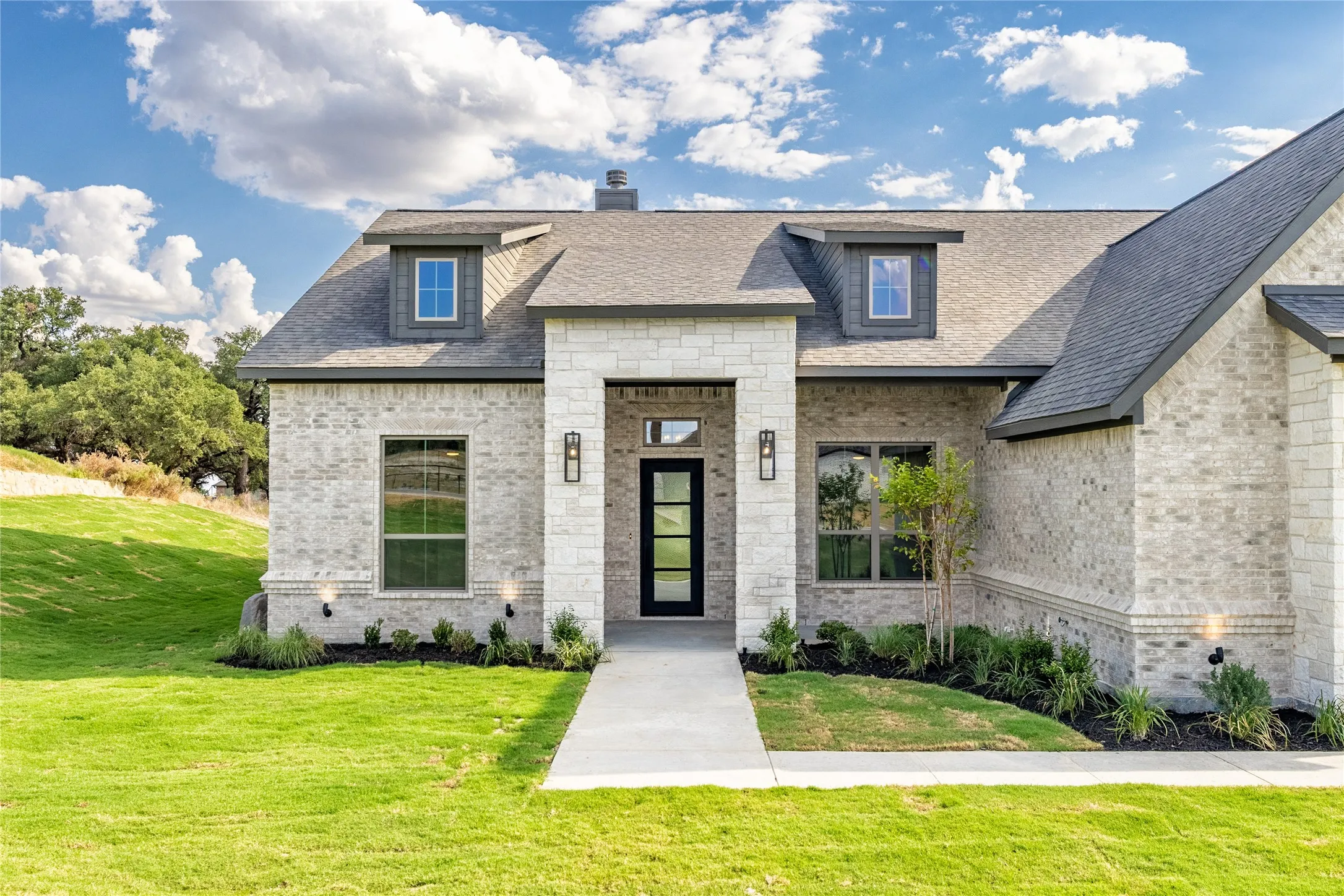 Brick and stone exterior with dormer windows, a covered entry, and a prominent front door