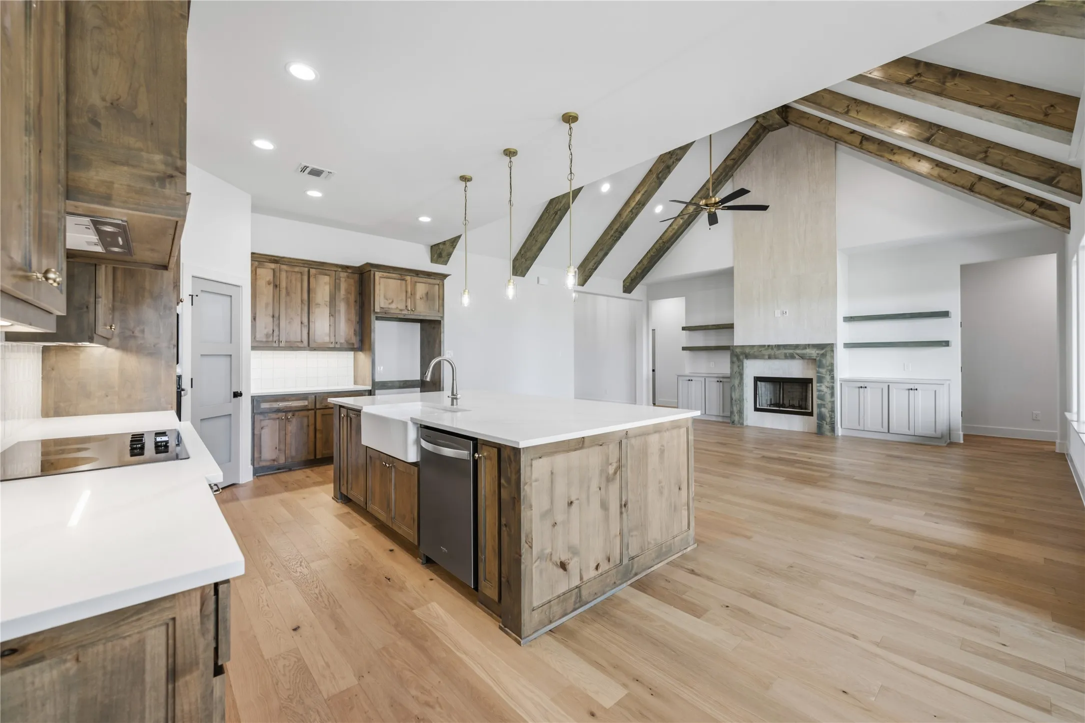 Kitchen and living area featuring a vaulted ceiling with exposed wood beams, hardwood flooring, and a fireplace with a stone surround