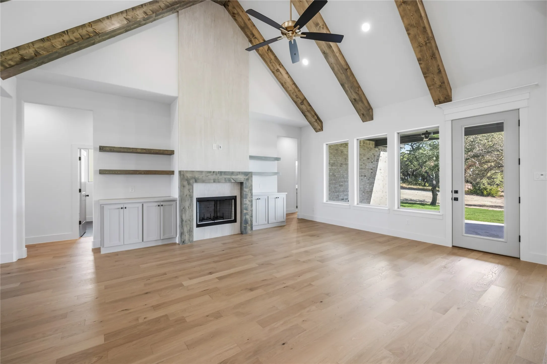 Vaulted ceilings with exposed wood beams, a stone fireplace, wood-finish flooring, built-in cabinetry, and multiple windows with exterior access