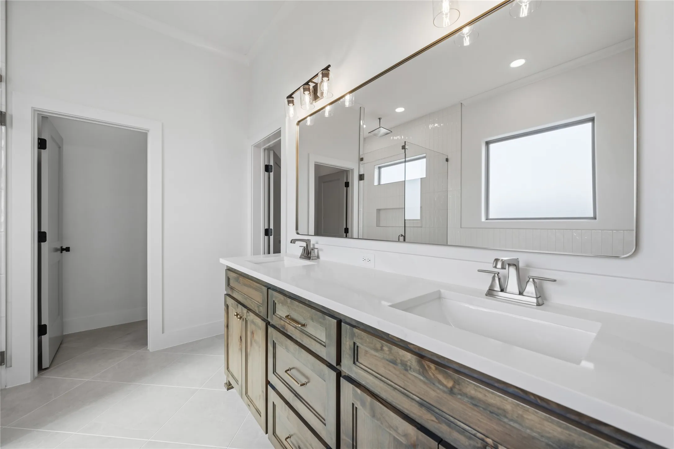Dual vanity with integrated sinks, white countertops, extensive mirror, and wood-finish cabinetry