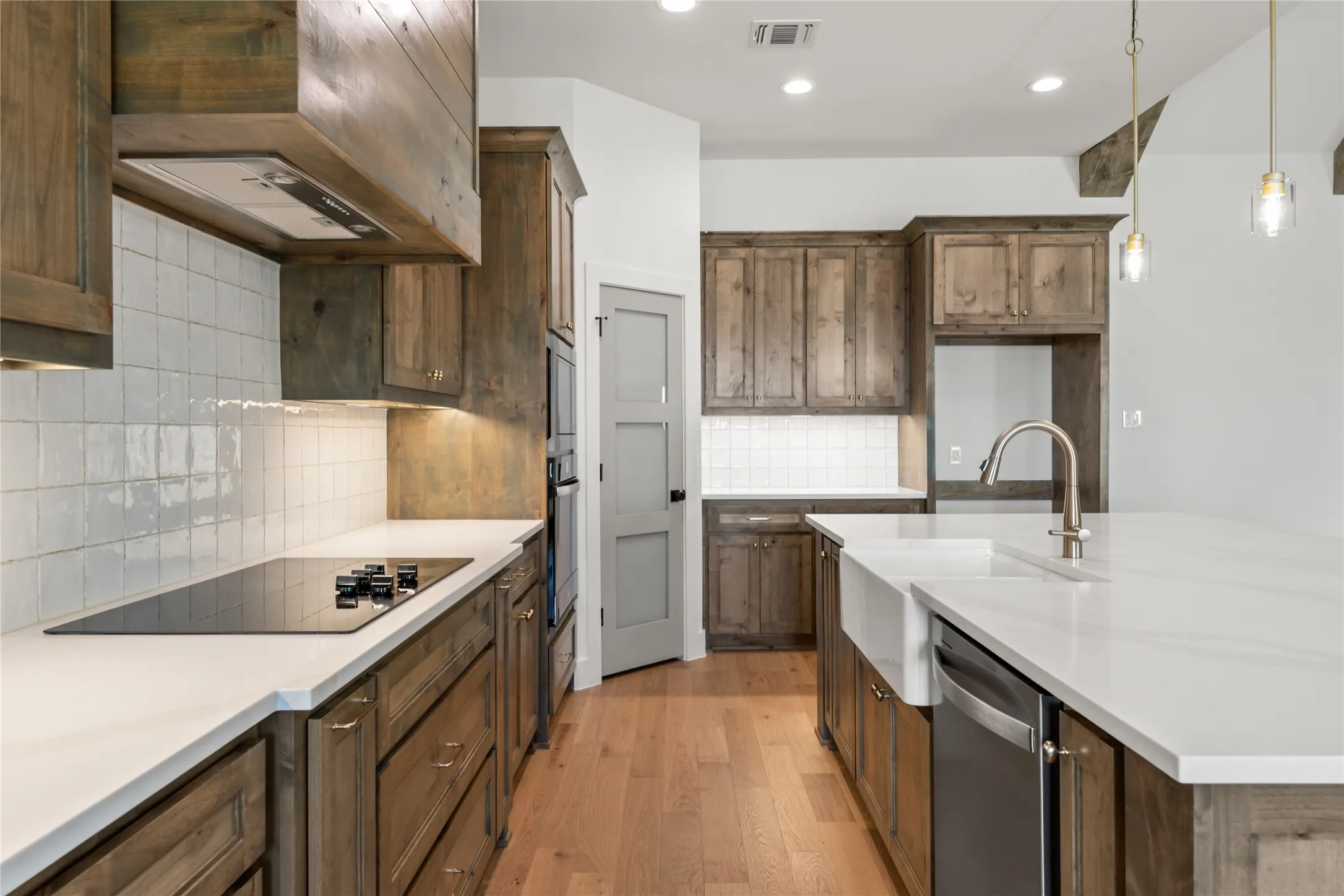 Kitchen featuring wood-finish cabinetry, white countertops, built-in cooktop, farm-style sink, and integrated dishwasher