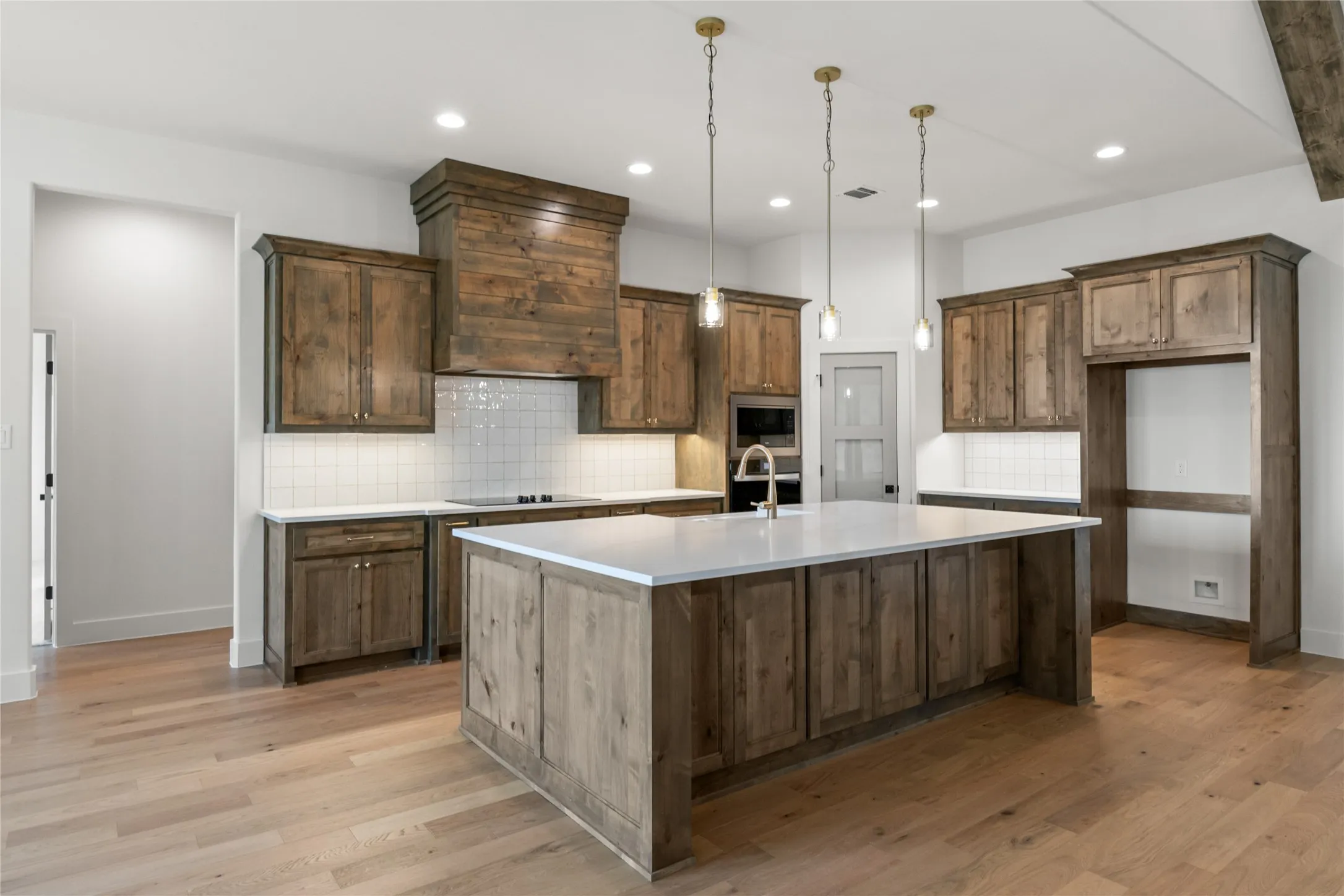 Kitchen featuring wood-finish cabinetry, a large center island with a light-toned countertop, integrated appliances, recessed lighting, and wood-finish flooring