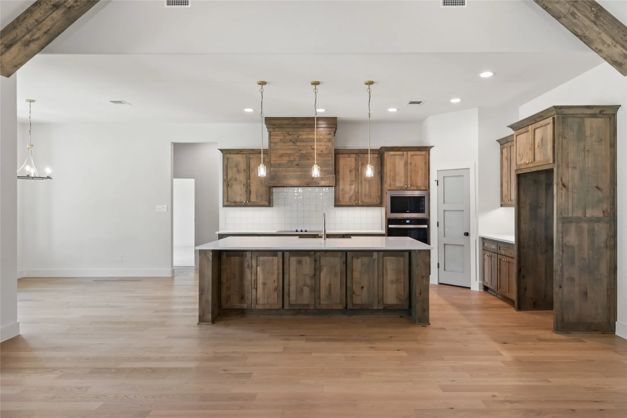 Open-concept kitchen with a large island, wood-finish cabinetry, integrated stainless steel appliances, and wood-finish flooring