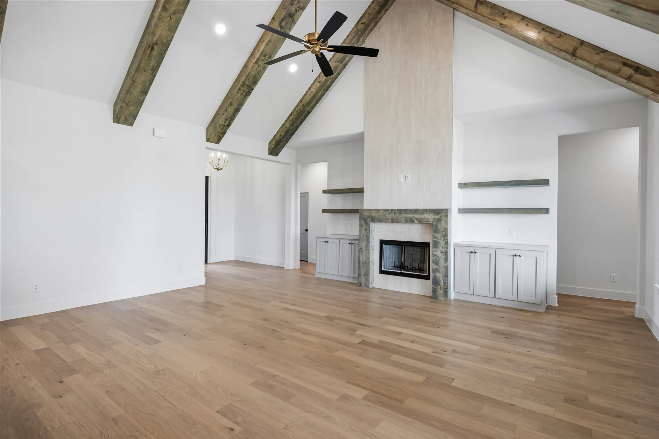 Vaulted ceiling with exposed wood beams, wood-finish flooring, built-in cabinetry, decorative fireplace with stone surround, and ceiling fan