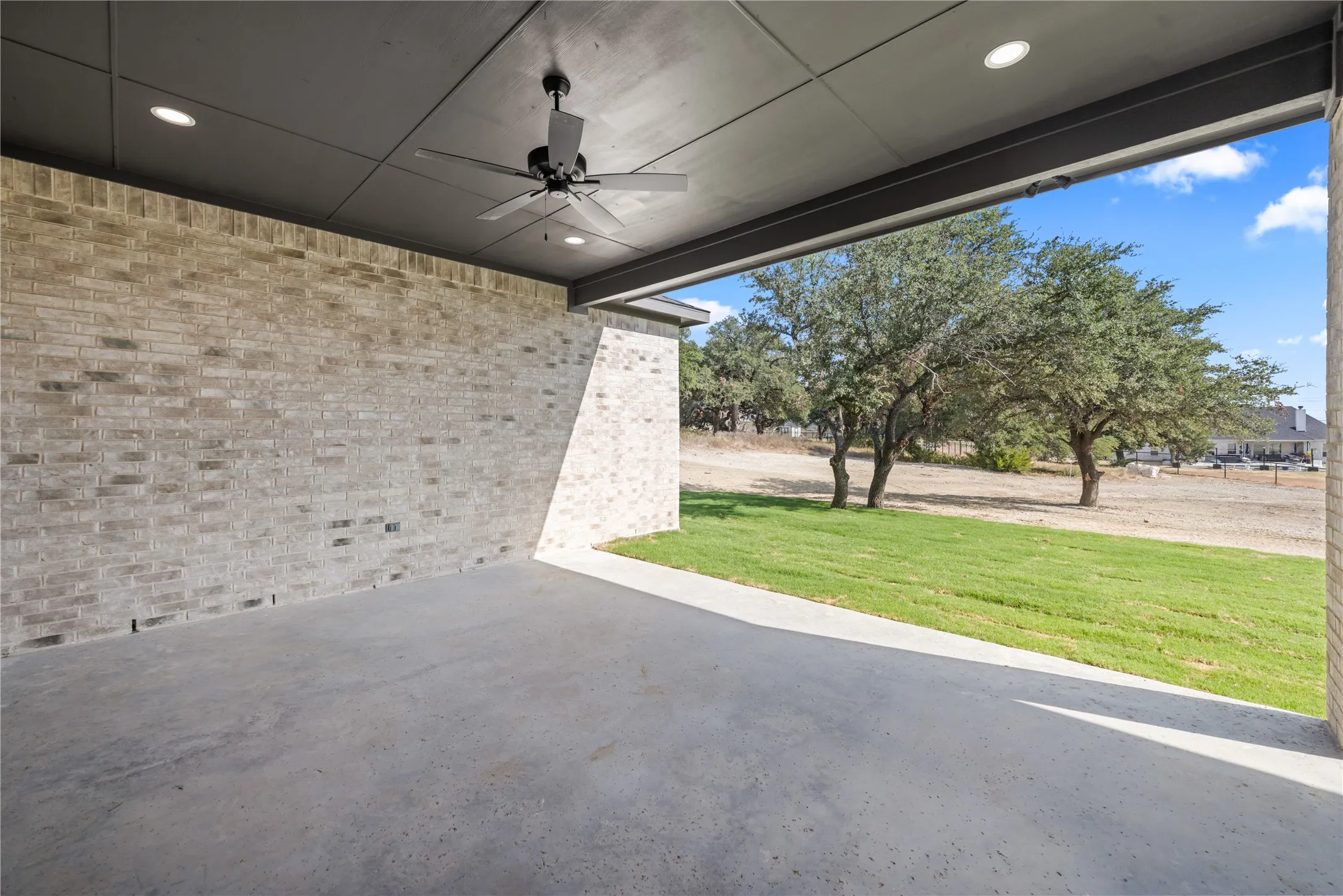Covered concrete patio with recessed lighting, ceiling fan, and brick exterior walls