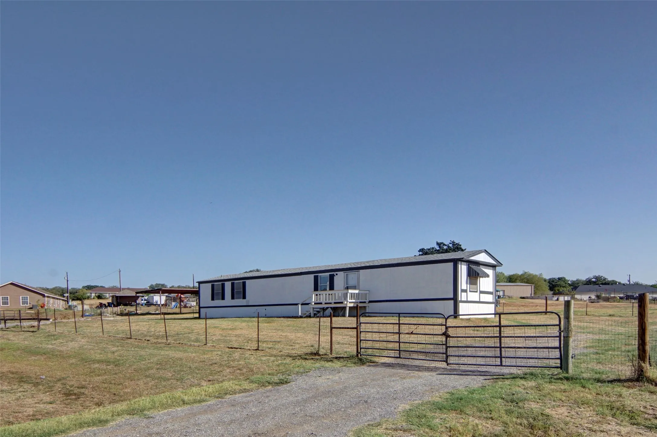 White siding exterior with dark trim, fenced perimeter, and a gravel driveway