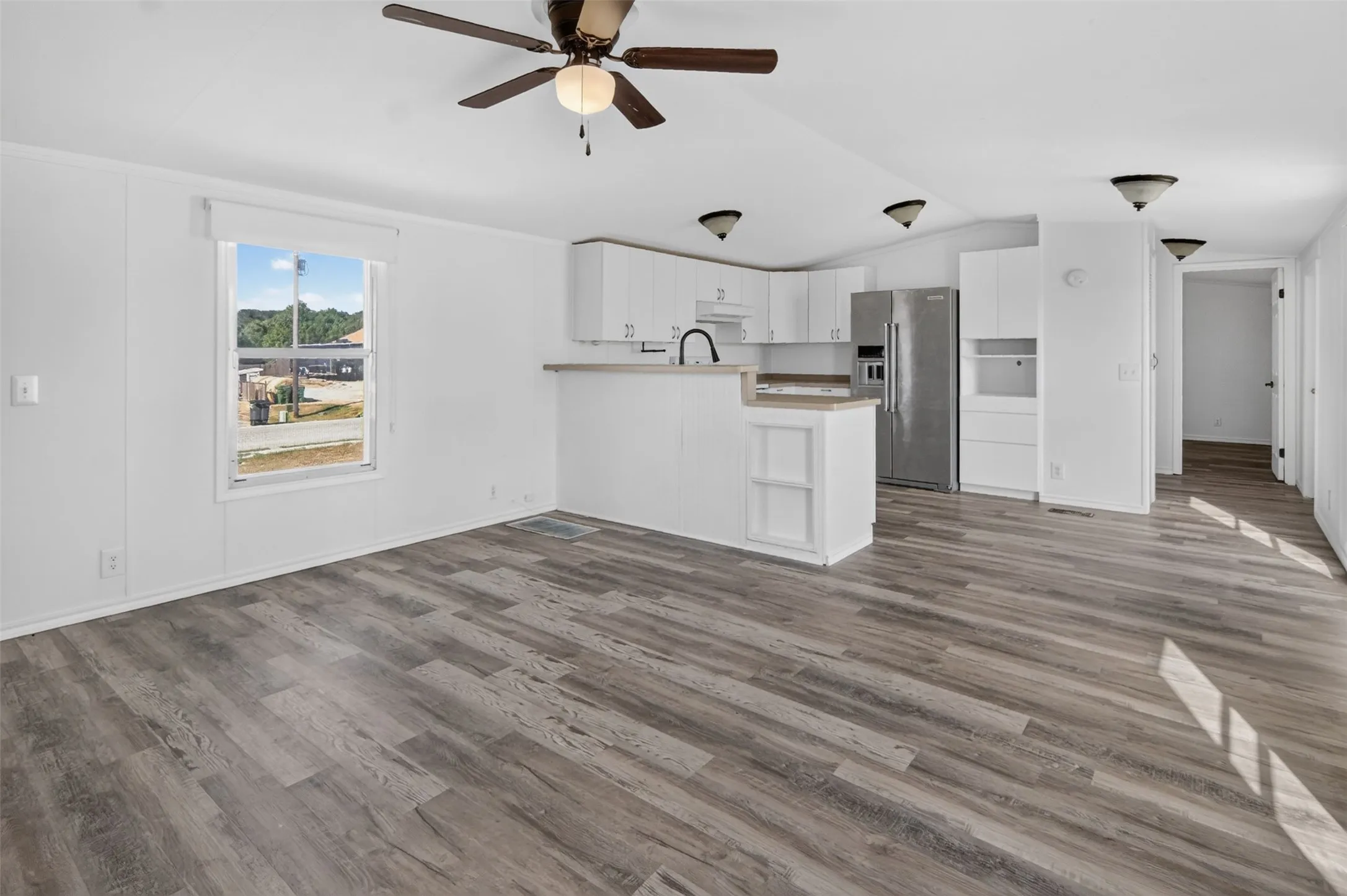 Expansive open-concept living area with wood-finish flooring, white cabinetry, and stainless steel appliances