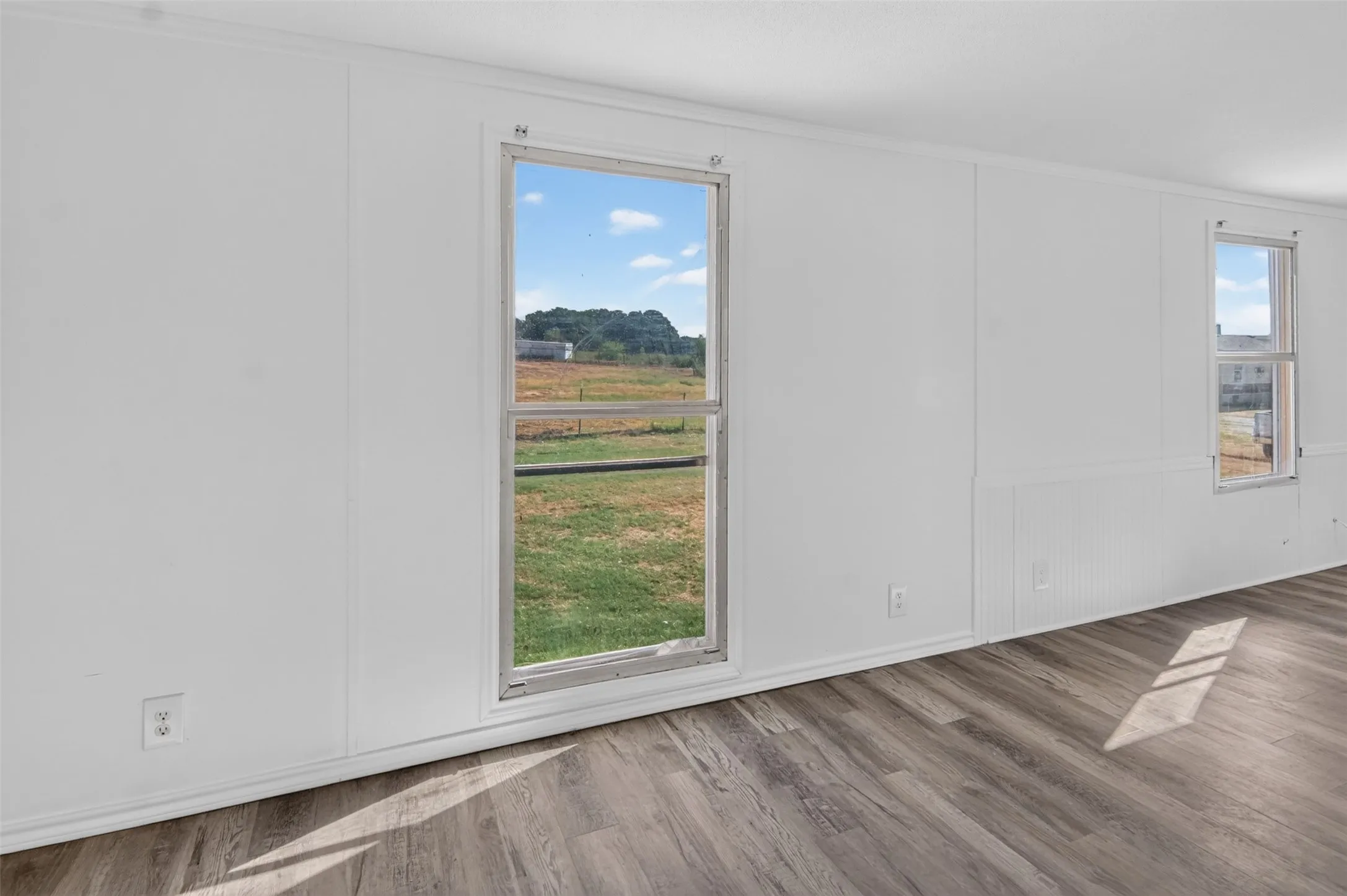 Wood-finish flooring with white baseboards, white wall paneling, and two windows