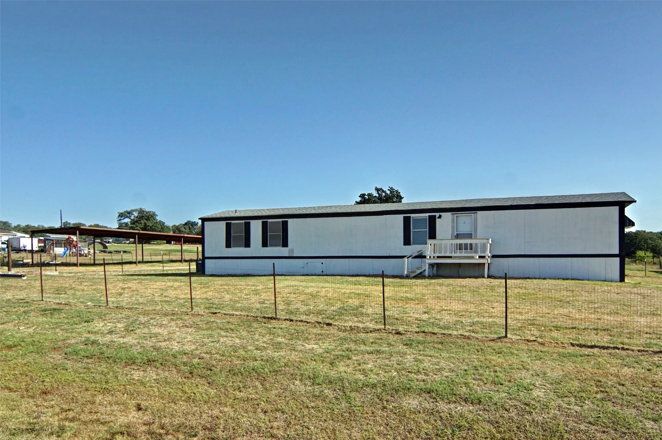 White exterior siding, dark roof, front porch, and an attached carport