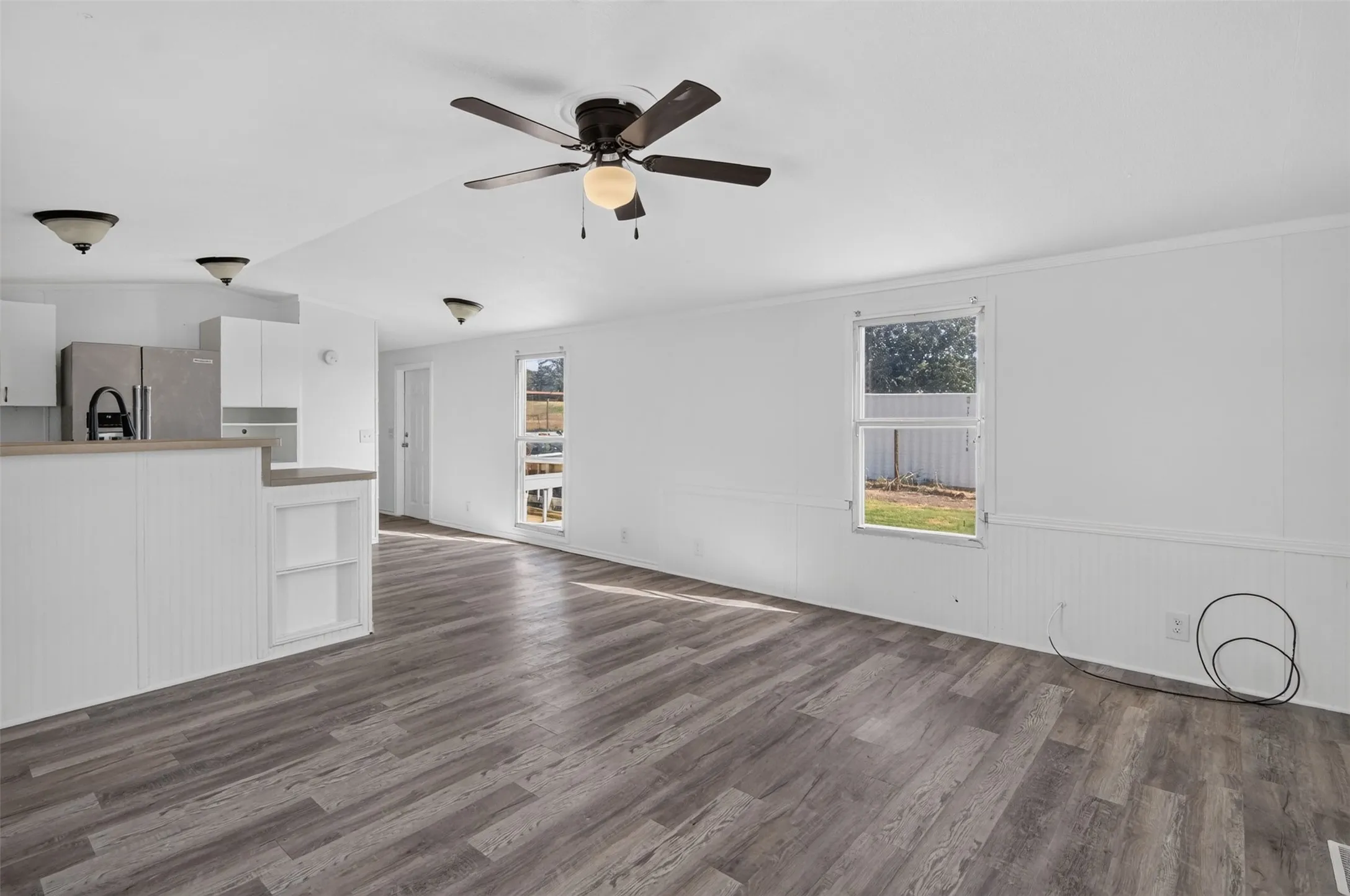 Open-concept living area with wood-finish flooring, white walls, and a ceiling fan